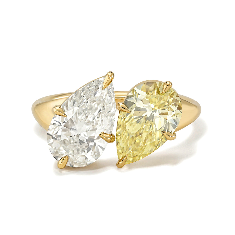 A yellow gold ring featuring two pear-cut diamonds, one white and one yellow, set on a plain white background.