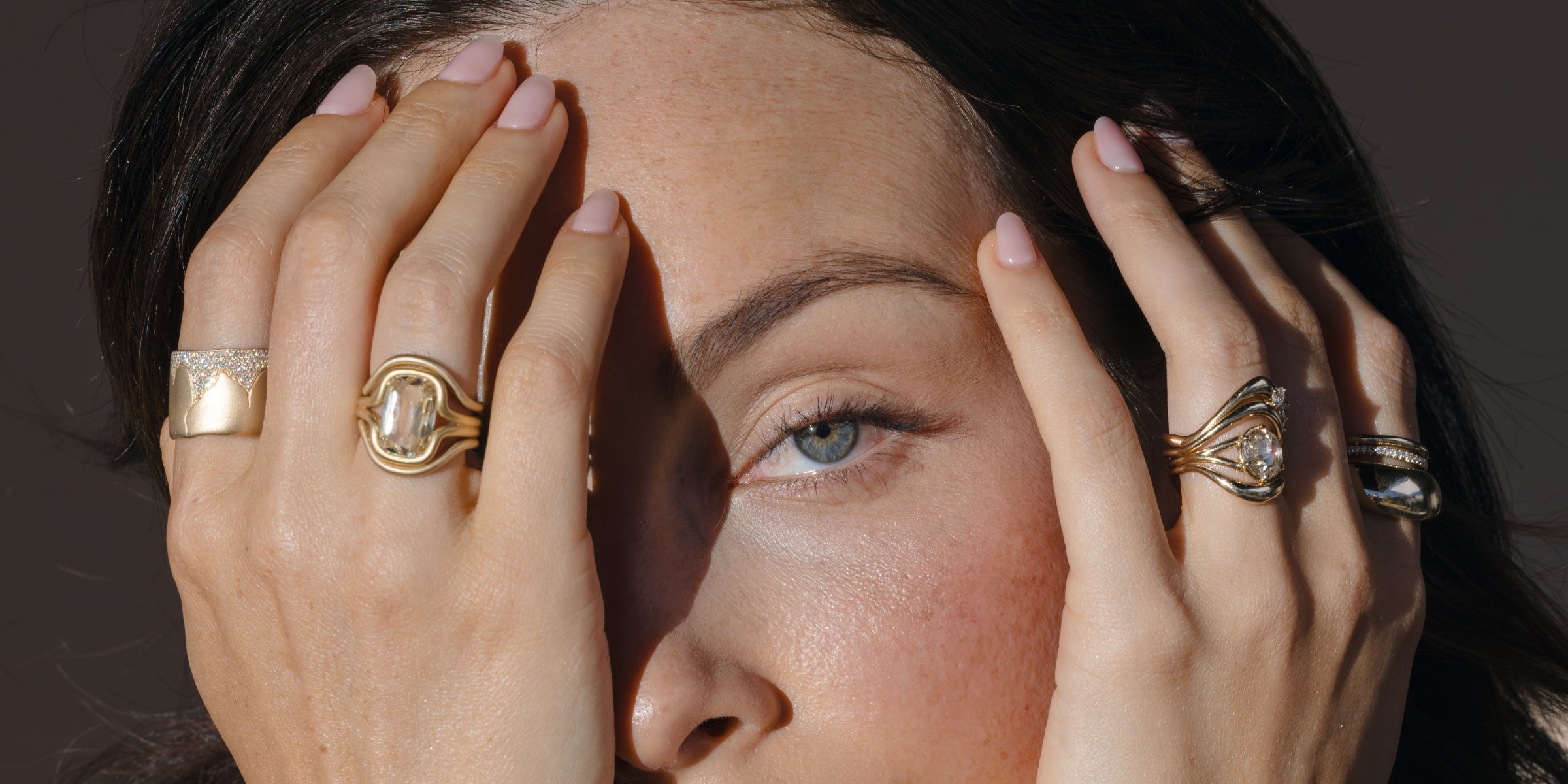 Hands display a unique engagement ring with a gold oval stone, plus matching bands on a woman.