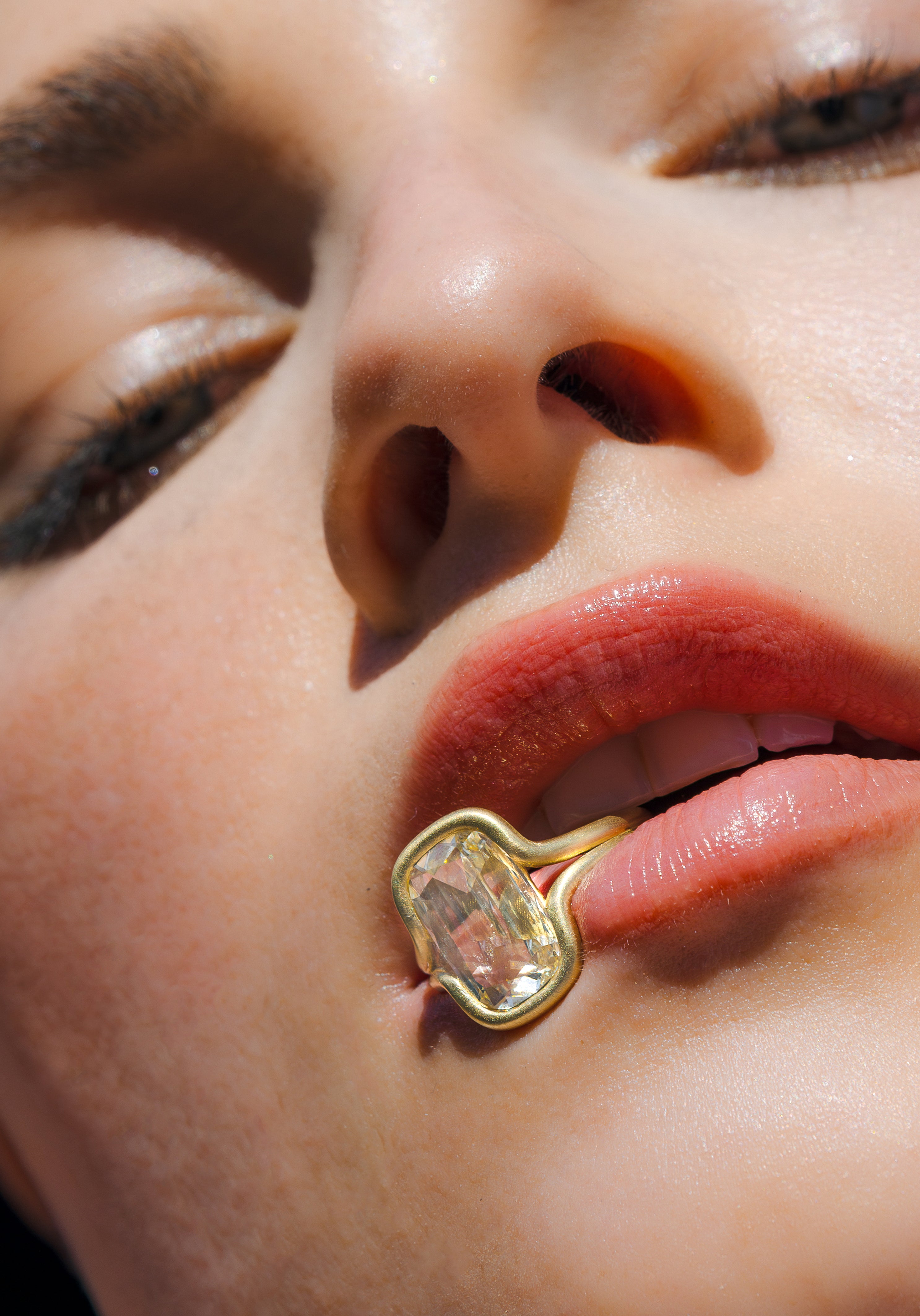 Unique engagement ring with a teardrop stone rests near lips in a close-up portrait with warm light