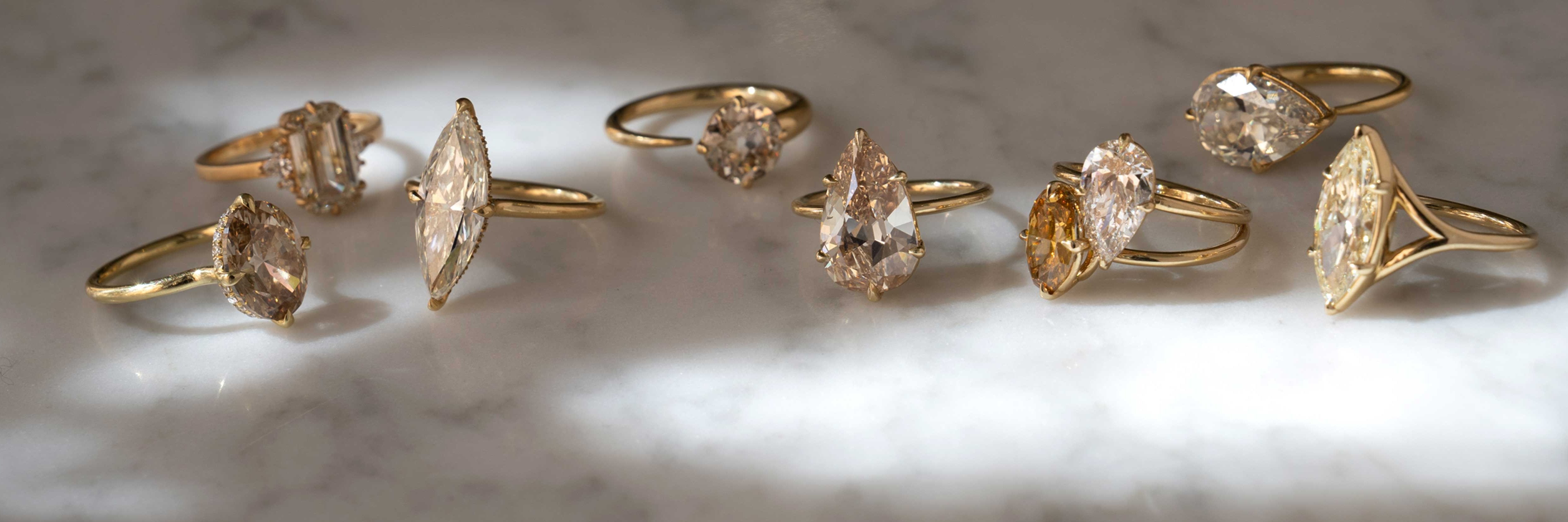 Gold diamond unique engagement ring designs with marquise and oval stones, asymmetrical settings on a neutral background