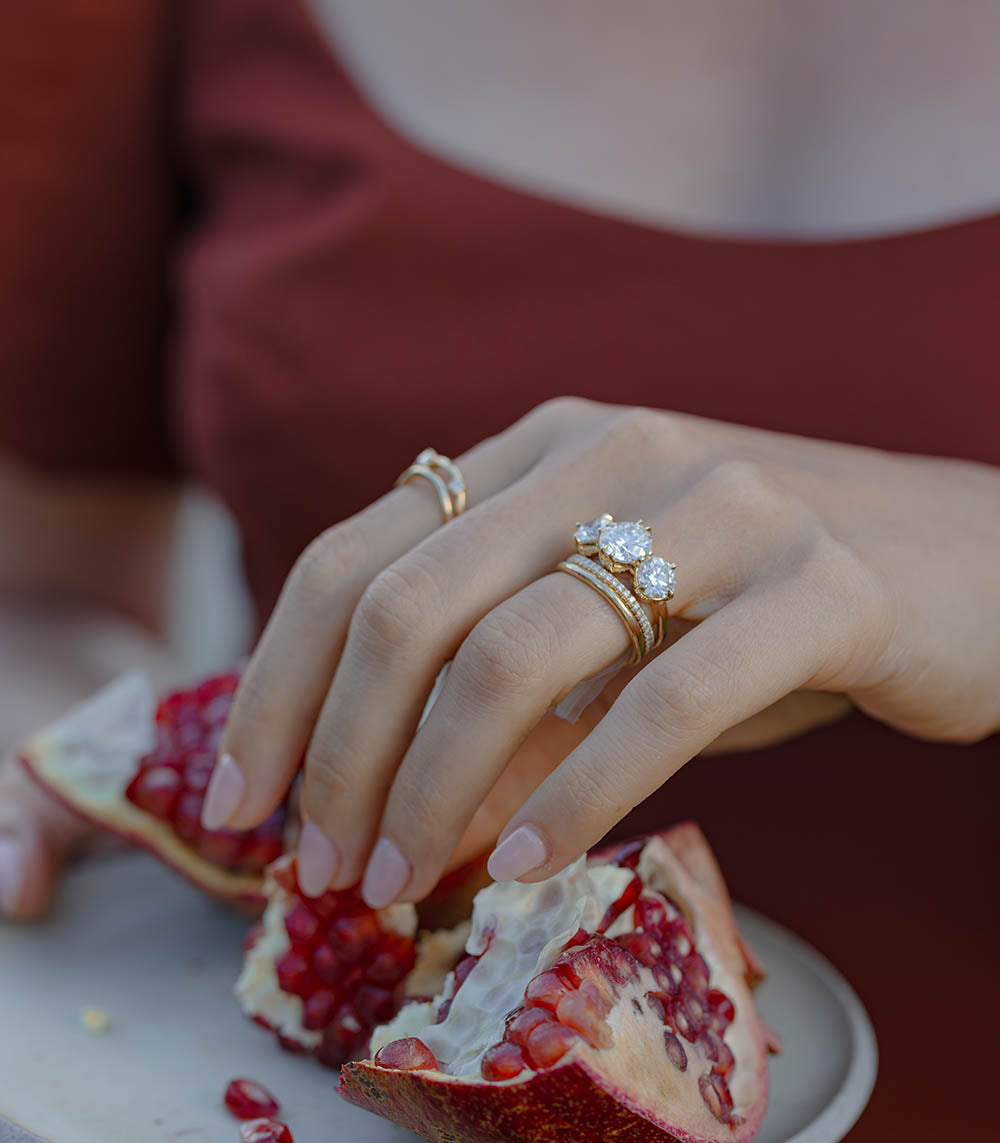Unique engagement ring, a 3 stone diamond ring on a hand, gold band with sparkling stones over red fruit