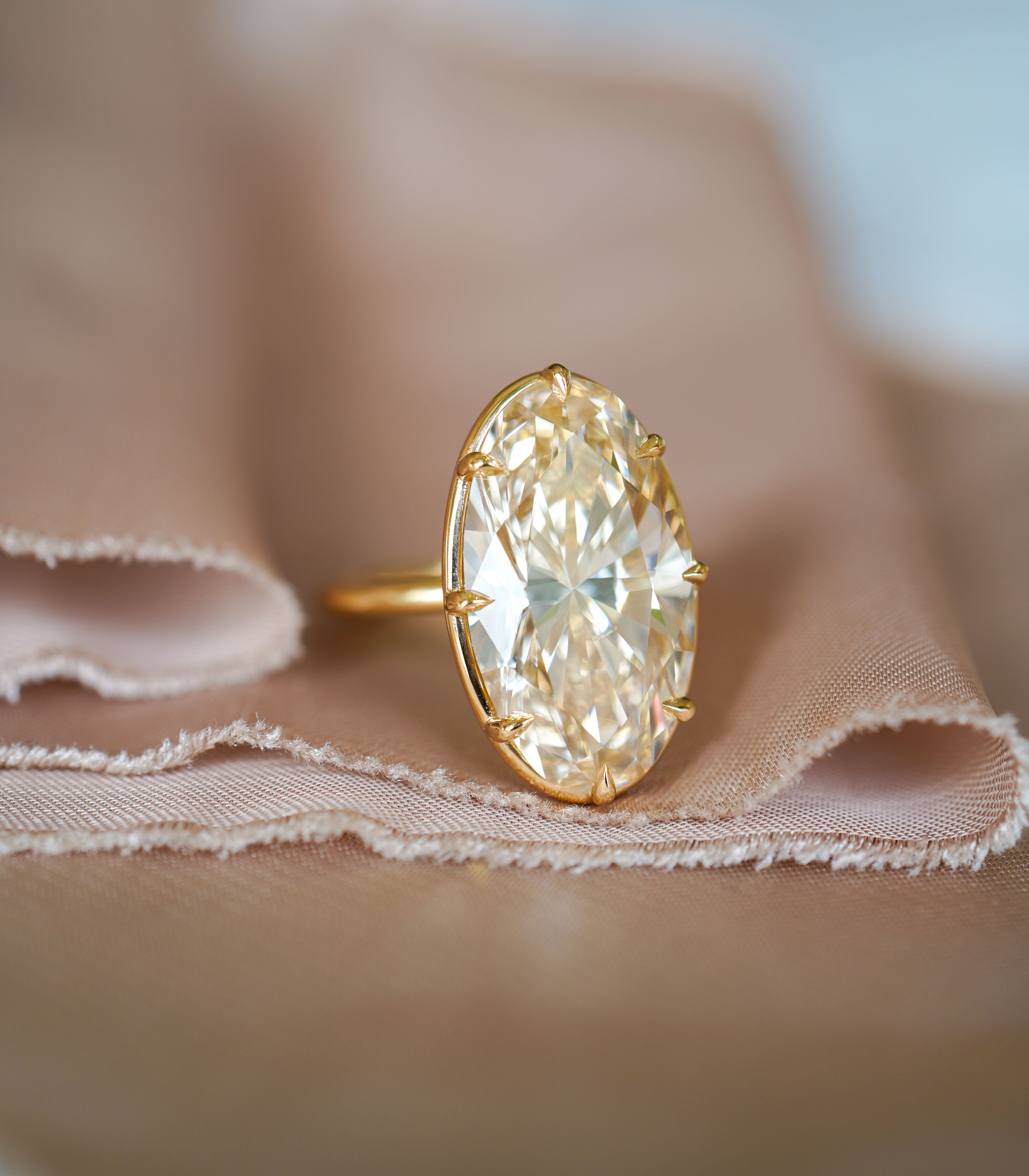 Unique engagement ring with a large oval diamond, gold prongs and an understated sparkle on fabric.