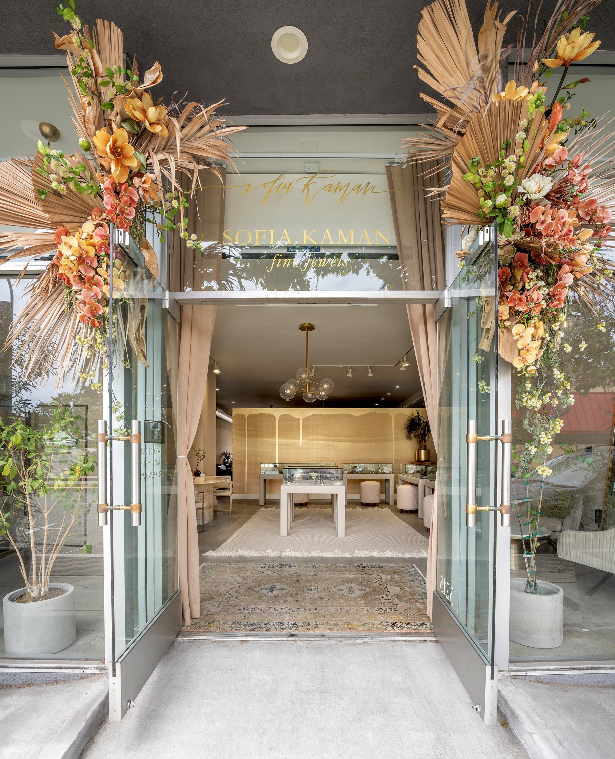 Understated shop entrance with floral and reed arches framing a jewelry display doorway and sign lettering