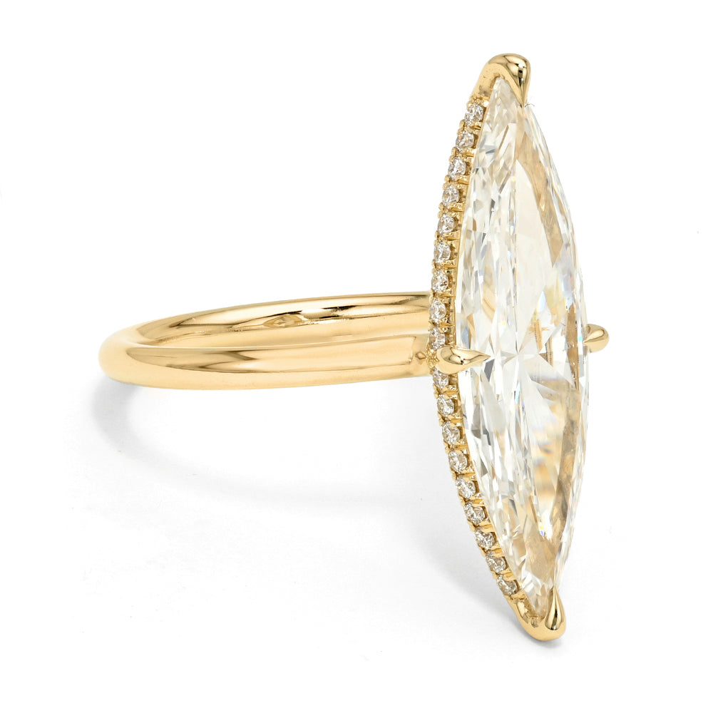 A yellow gold ring featuring a large marquise-cut diamond in a prong setting, accented by small pavé diamonds along the side of the stone, shown on a white background.