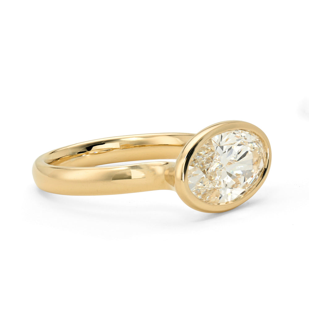 A yellow gold bezel-set elongated oval diamond ring, shown on a plain white background.