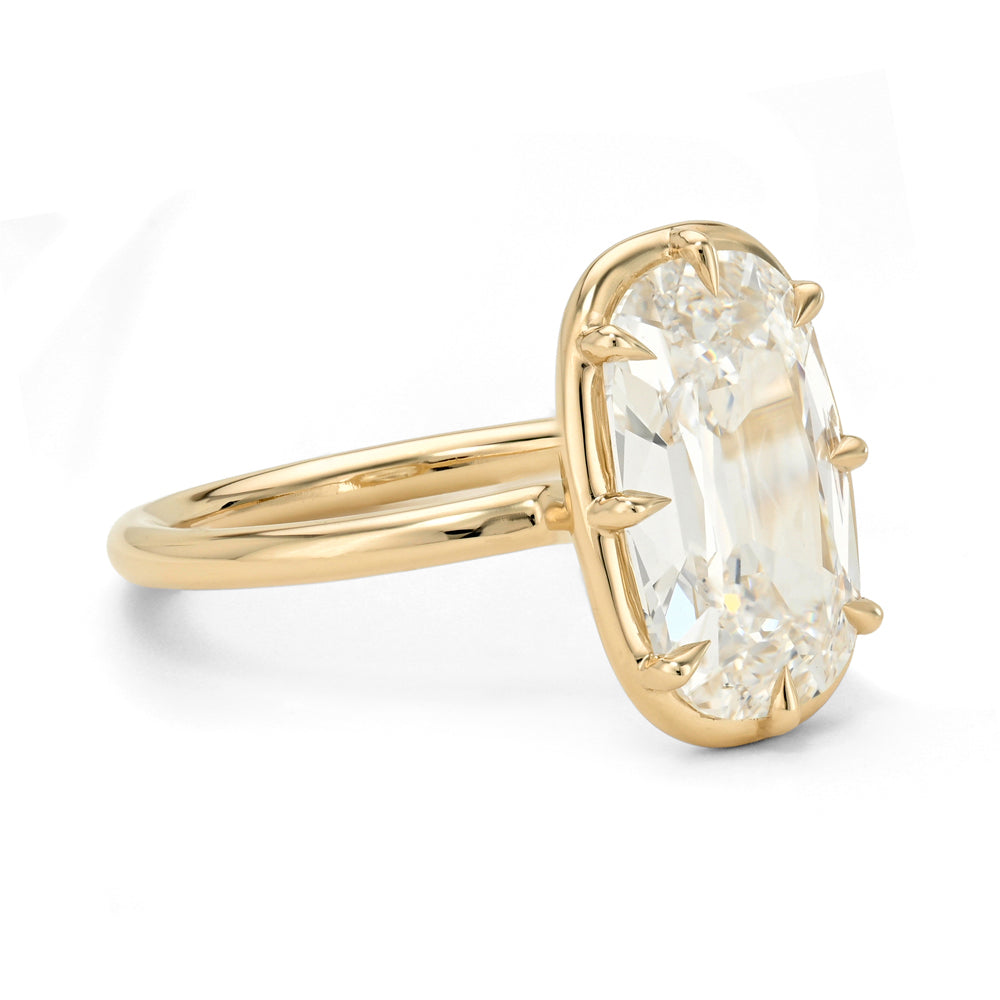 A yellow gold ring featuring a large, cushion-cut clear gemstone in a prong setting, shown on a clean white background.