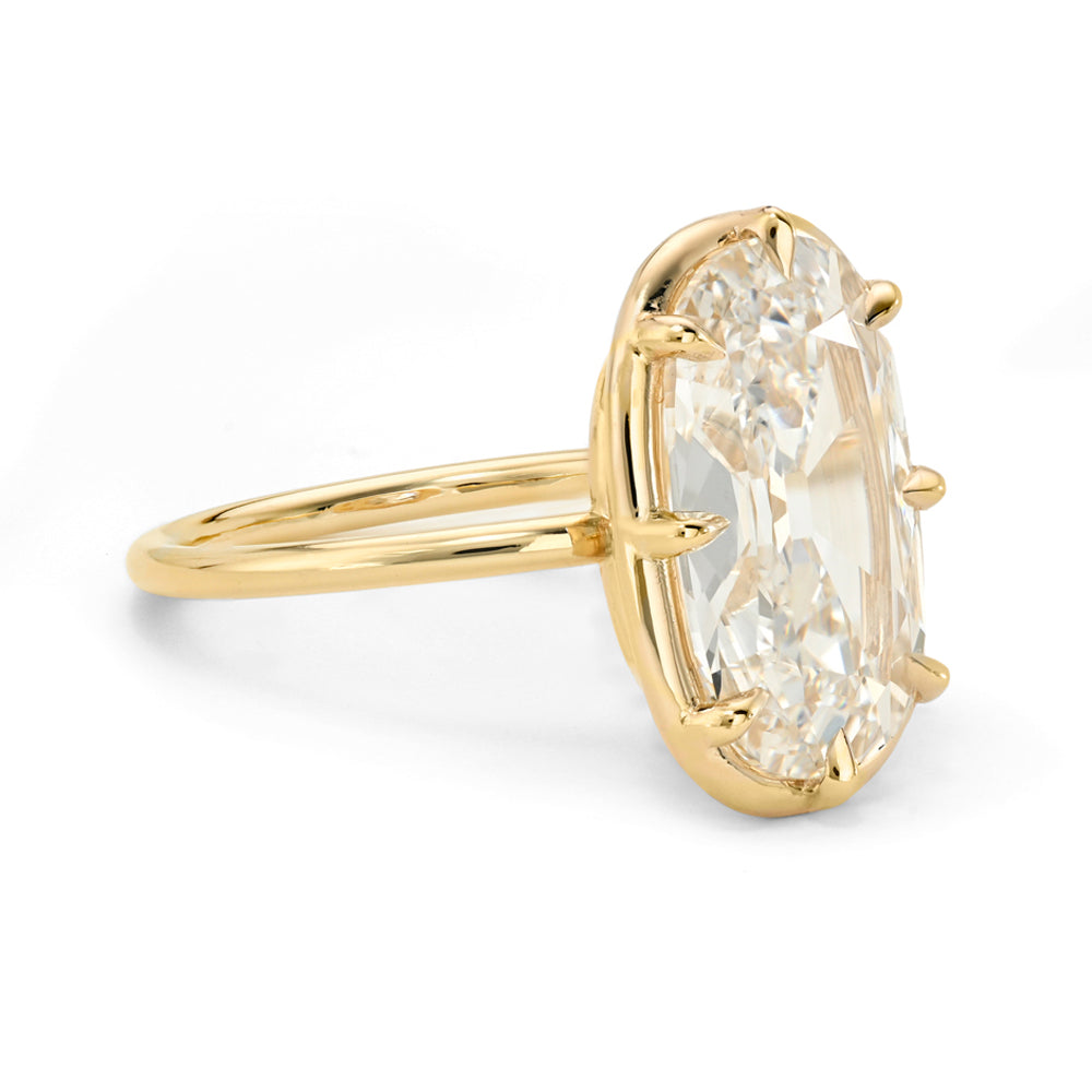 A yellow gold ring featuring a large, flat elongated cushion old mine-cut diamond in a prong setting, shown on a clean white background.