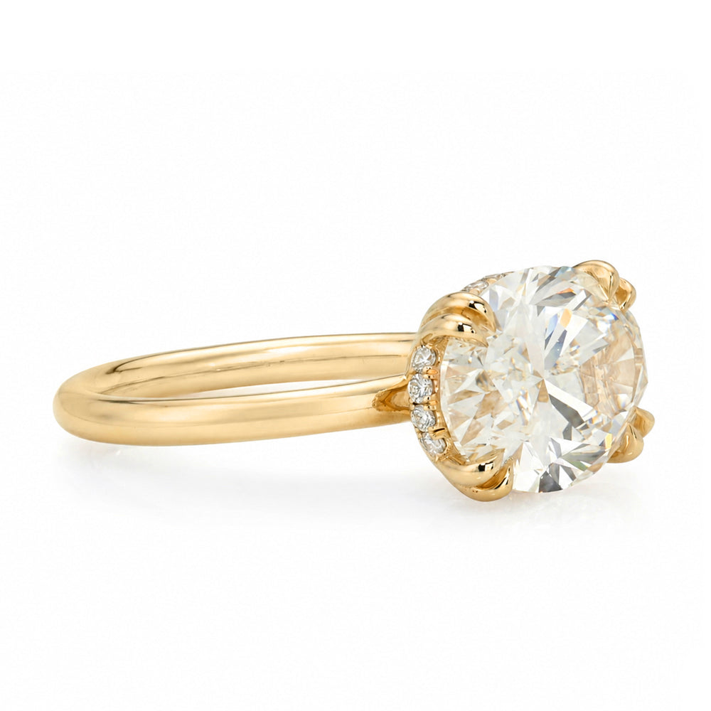 A yellow gold solitaire engagement ring featuring a oval brilliant cut white diamond set east west in a prong setting with a hidden halo on the basket and double prongs, shown on a clean white background.