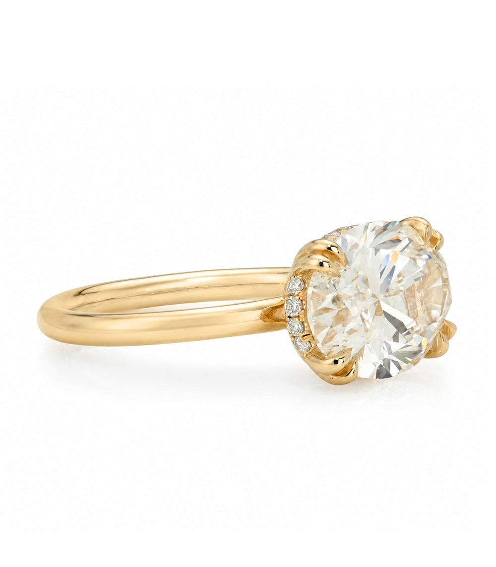 A yellow gold solitaire engagement ring featuring a oval brilliant cut white diamond set east west in a prong setting with a hidden halo on the basket and double prongs, shown on a clean white background.