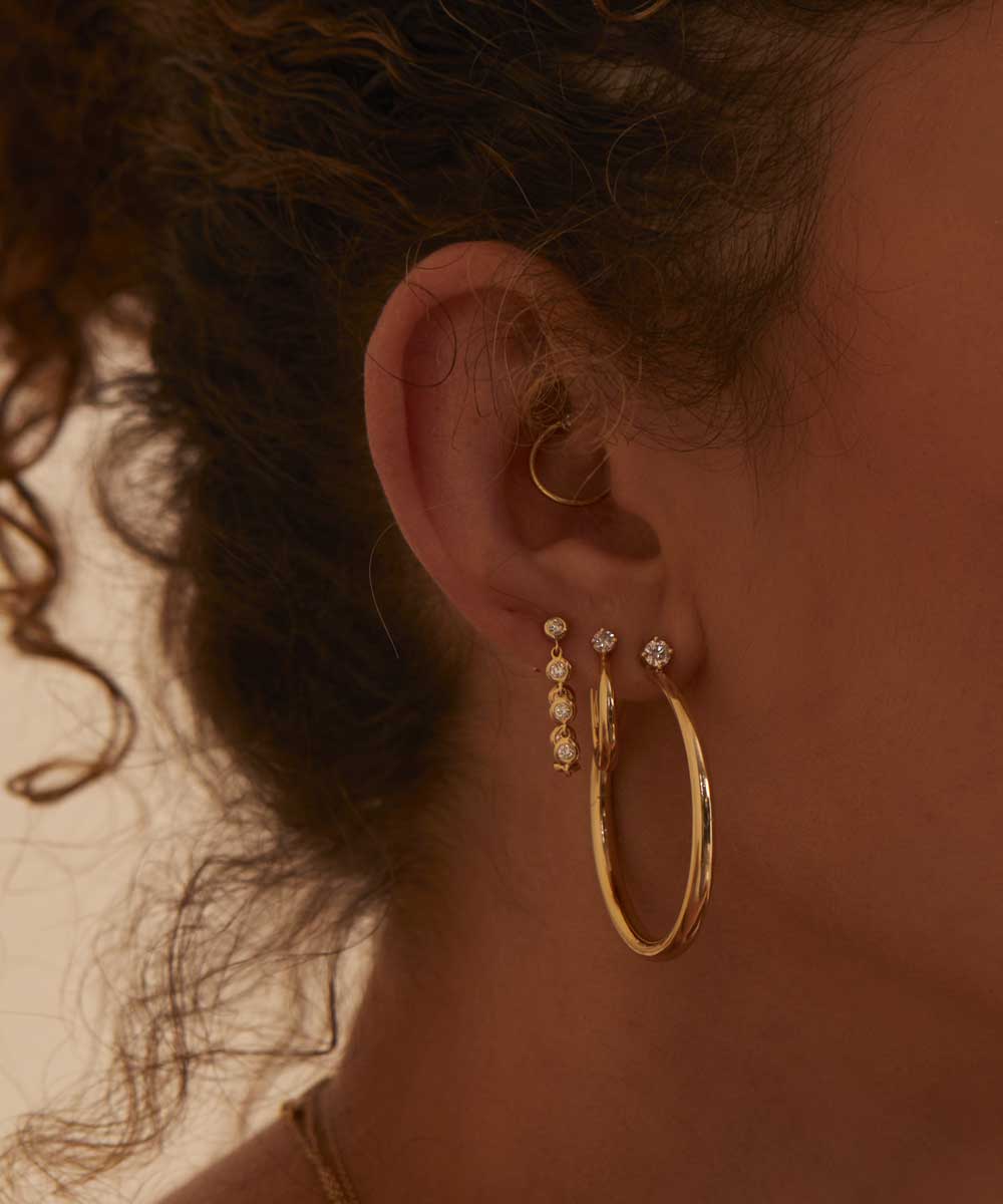 Woman’s ear with gold hoop and dangling charms in warm light, showing no ring on display
