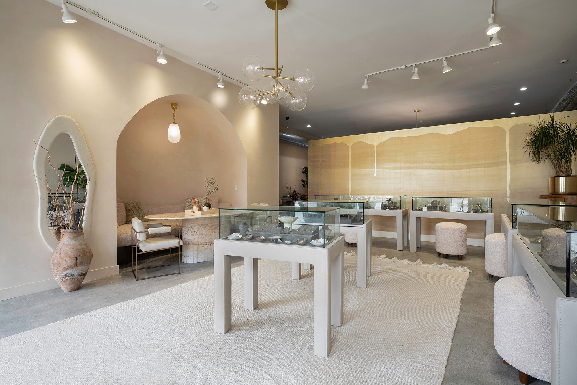 Bright jewelry showroom with glass display cases, pendant lights, and a seating area