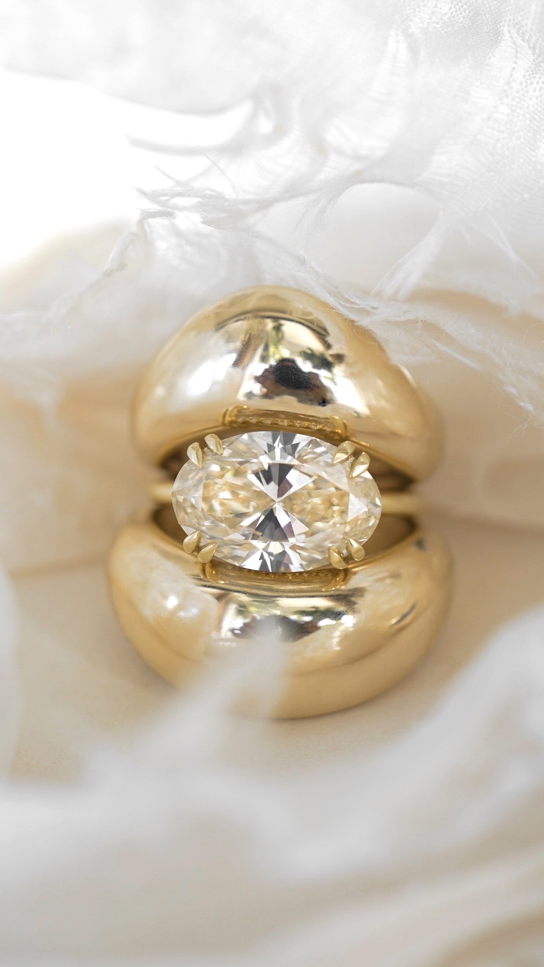 Unique engagement ring with gold band and large round diamond center on soft white textured background