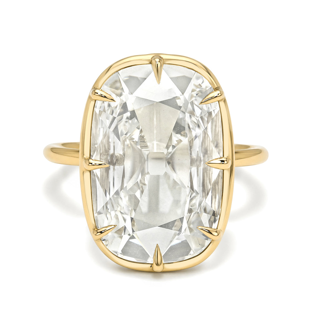 A yellow gold ring featuring a large, cushion-cut clear gemstone in a prong setting, shown against a plain white background.