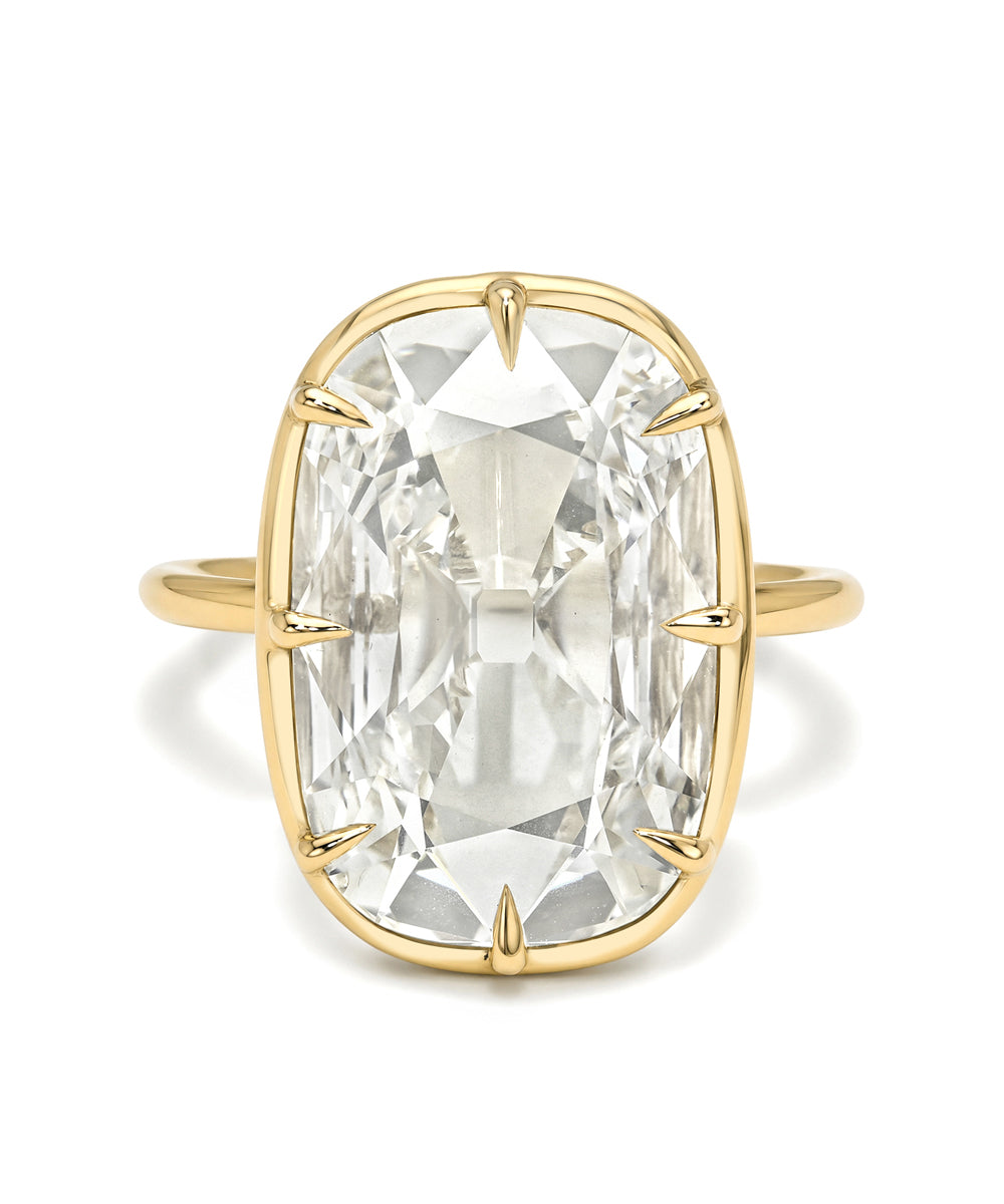A yellow gold ring featuring a large, cushion-cut clear gemstone in a prong setting, shown against a plain white background.