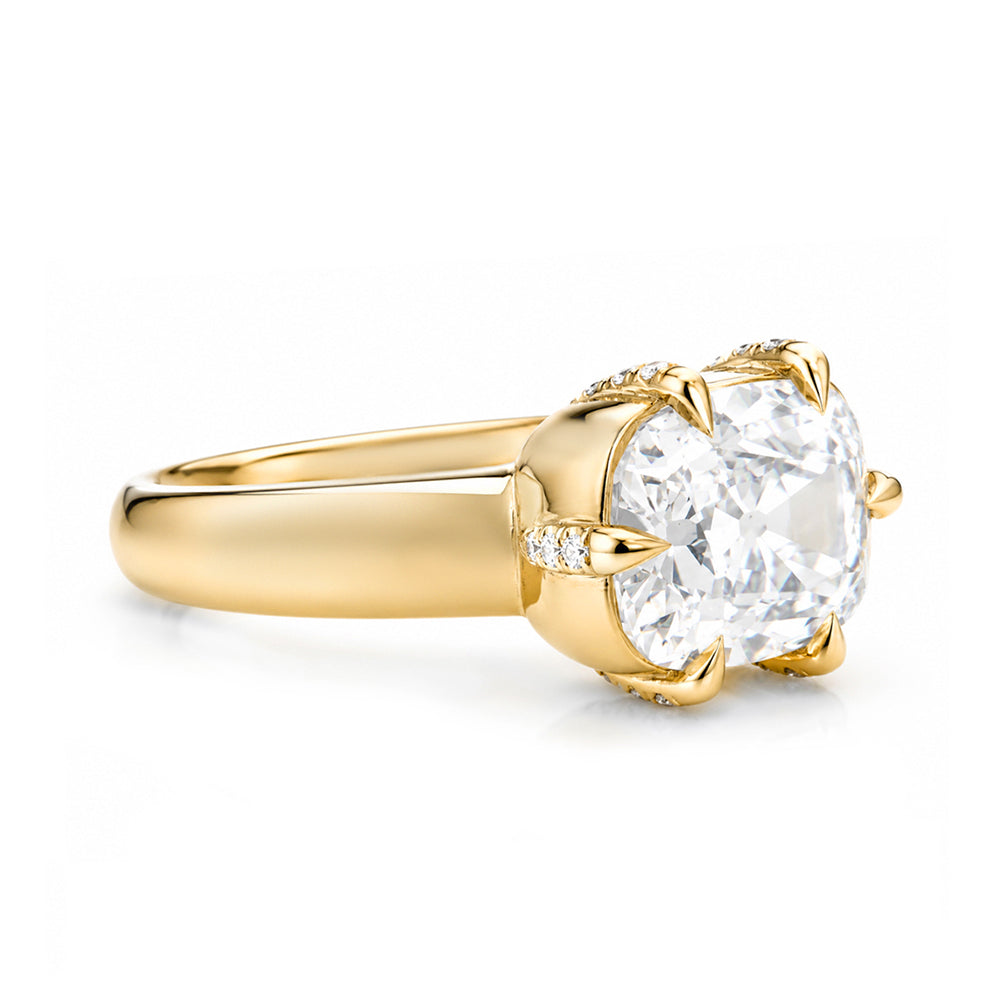 A yellow gold solitaire engagement ring featuring a large elongated cushion old mine-cut diamond center stone in a prong setting, with small pavé diamonds along the band, shown on a white background.