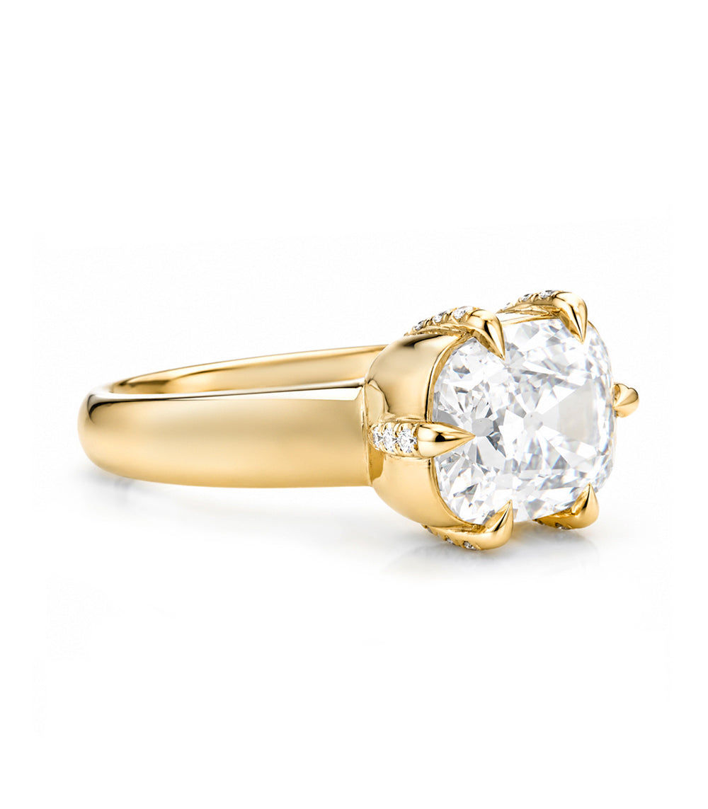 A yellow gold solitaire engagement ring featuring a large elongated cushion old mine-cut diamond center stone in a prong setting, with small pavé diamonds along the band, shown on a white background.