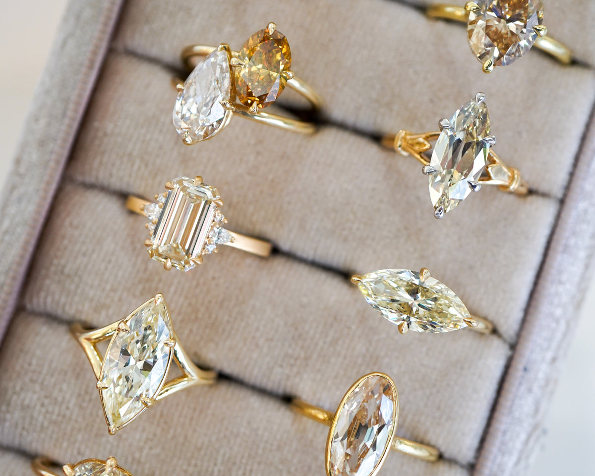 Unique engagement ring with a yellow center diamond on a gold band, beside other diamond rings.