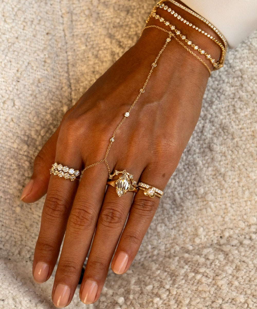 Isola engagement ring featuring a marquise old mine cut natural champagne diamond in yellow gold, styled with diamond rings, pinky rings, a delicate hand chain, and layered gold bracelets.