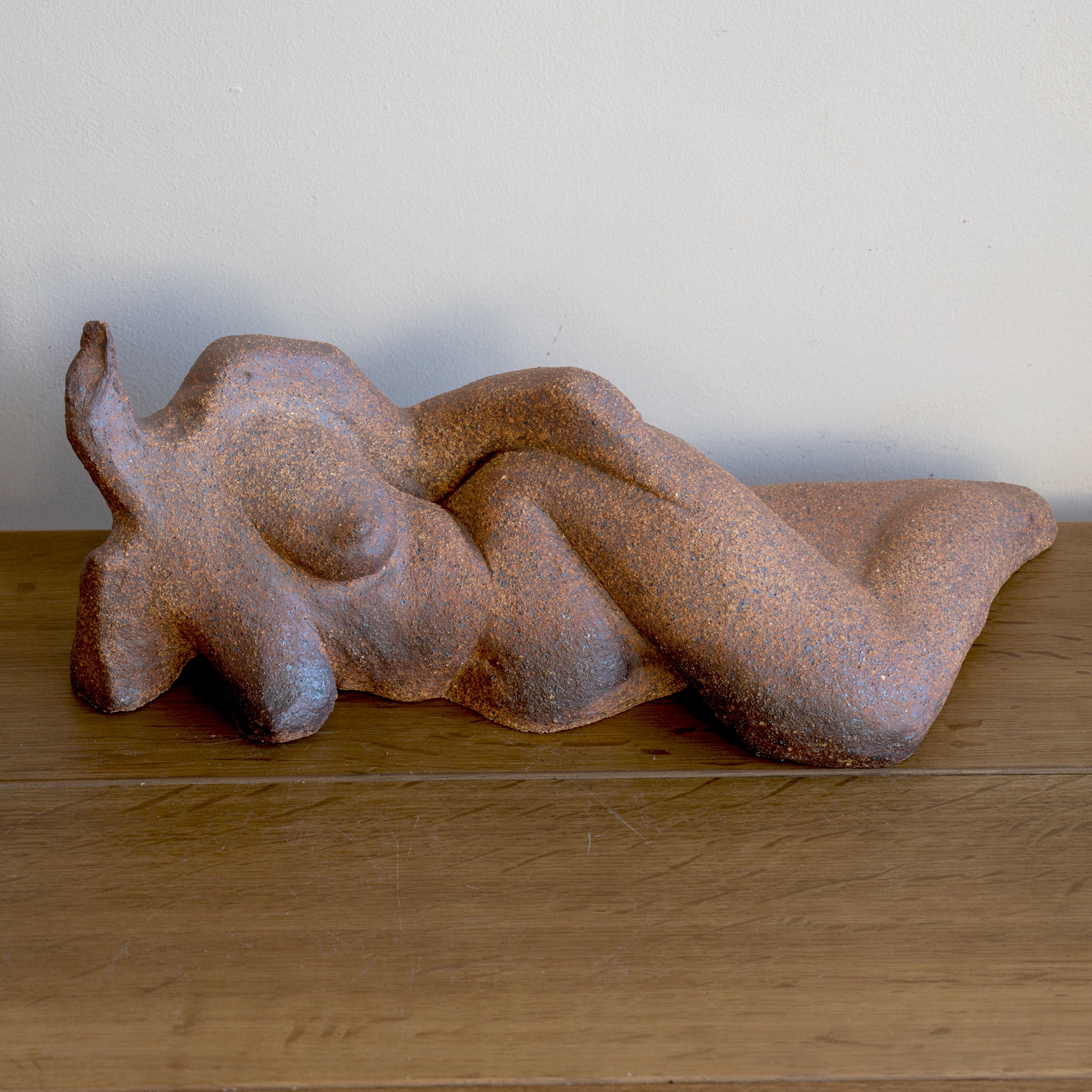 Lounging RM-008 sculpted rust-brown stone figurine on wooden table, textured surface against white wall.