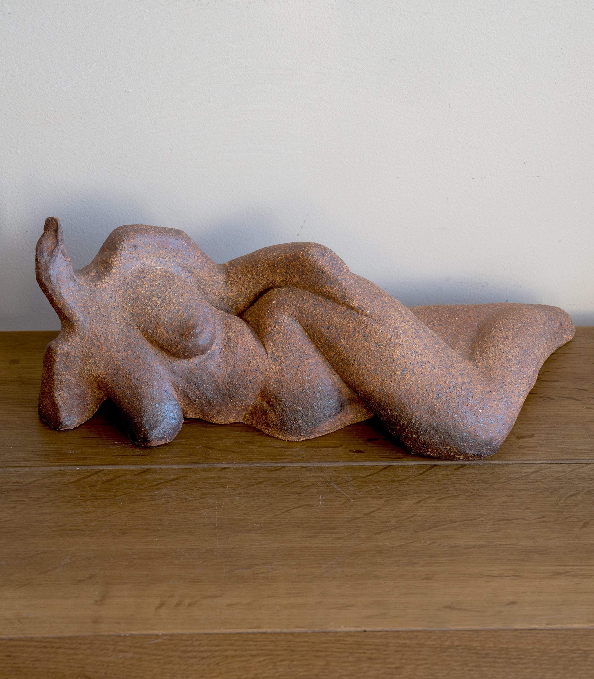 Lounging RM-008 sculpted rust-brown stone figurine on wooden table, textured surface against white wall.