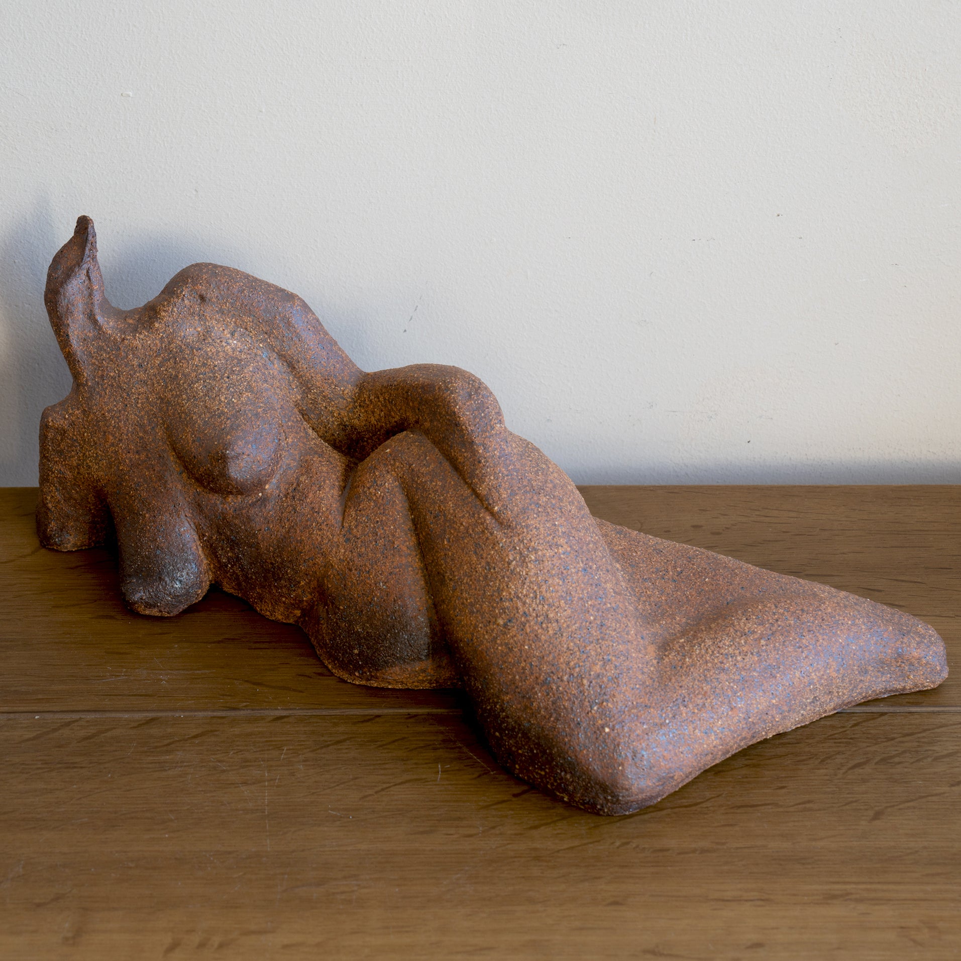 Lounging RM-008 stone sculpture in rust-brown with textured surface, resting on wooden floor