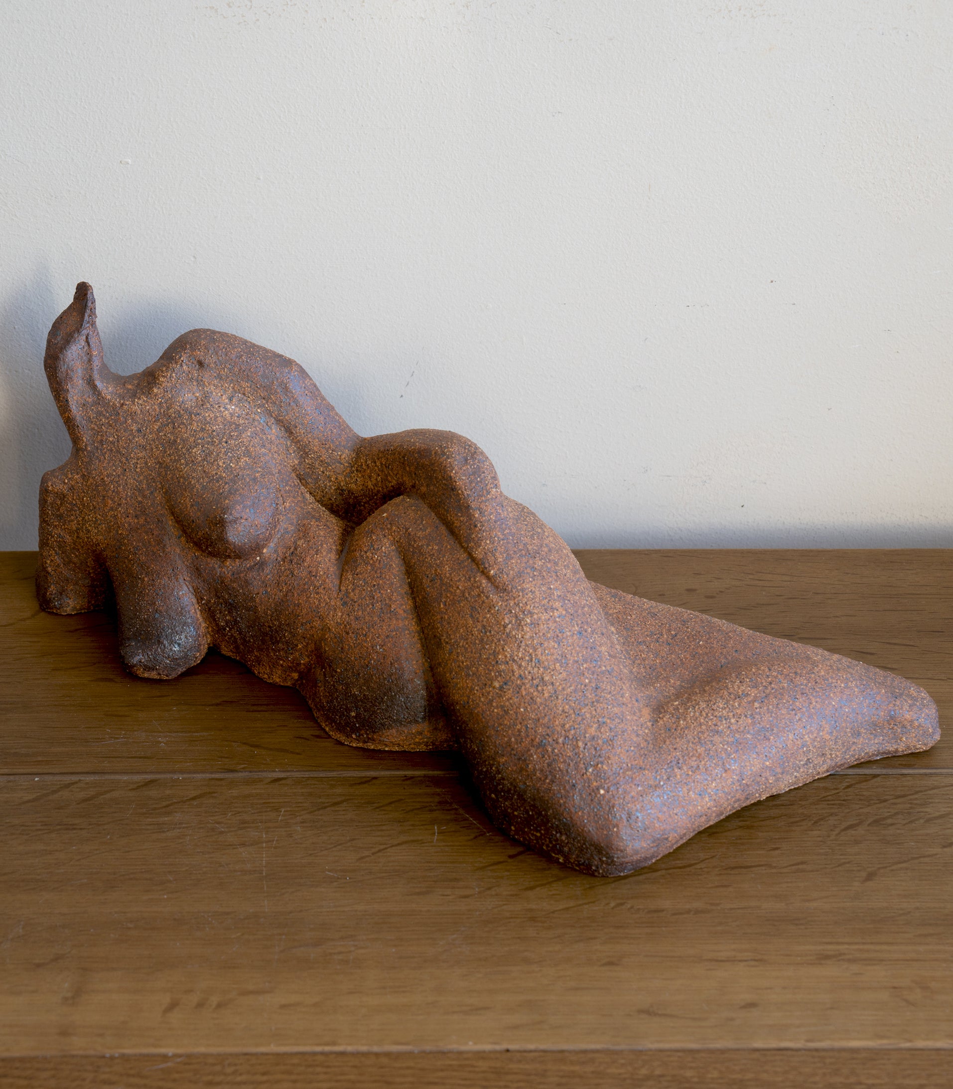 Lounging RM-008 stone sculpture in rust-brown with textured surface, resting on wooden floor