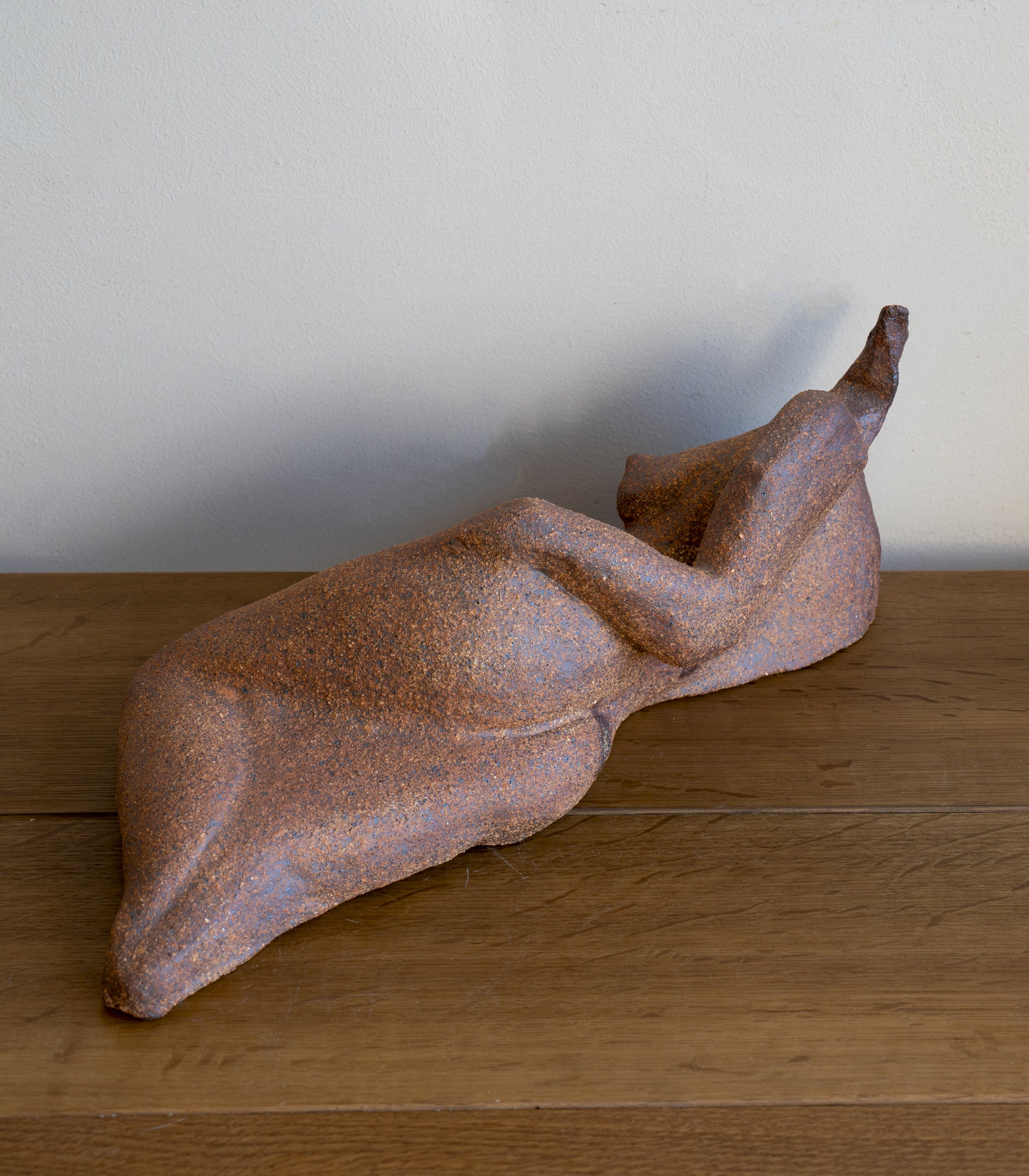 Lounging RM-008 rust-brown speckled stone sculpture, smooth lounging pose against pale wall.