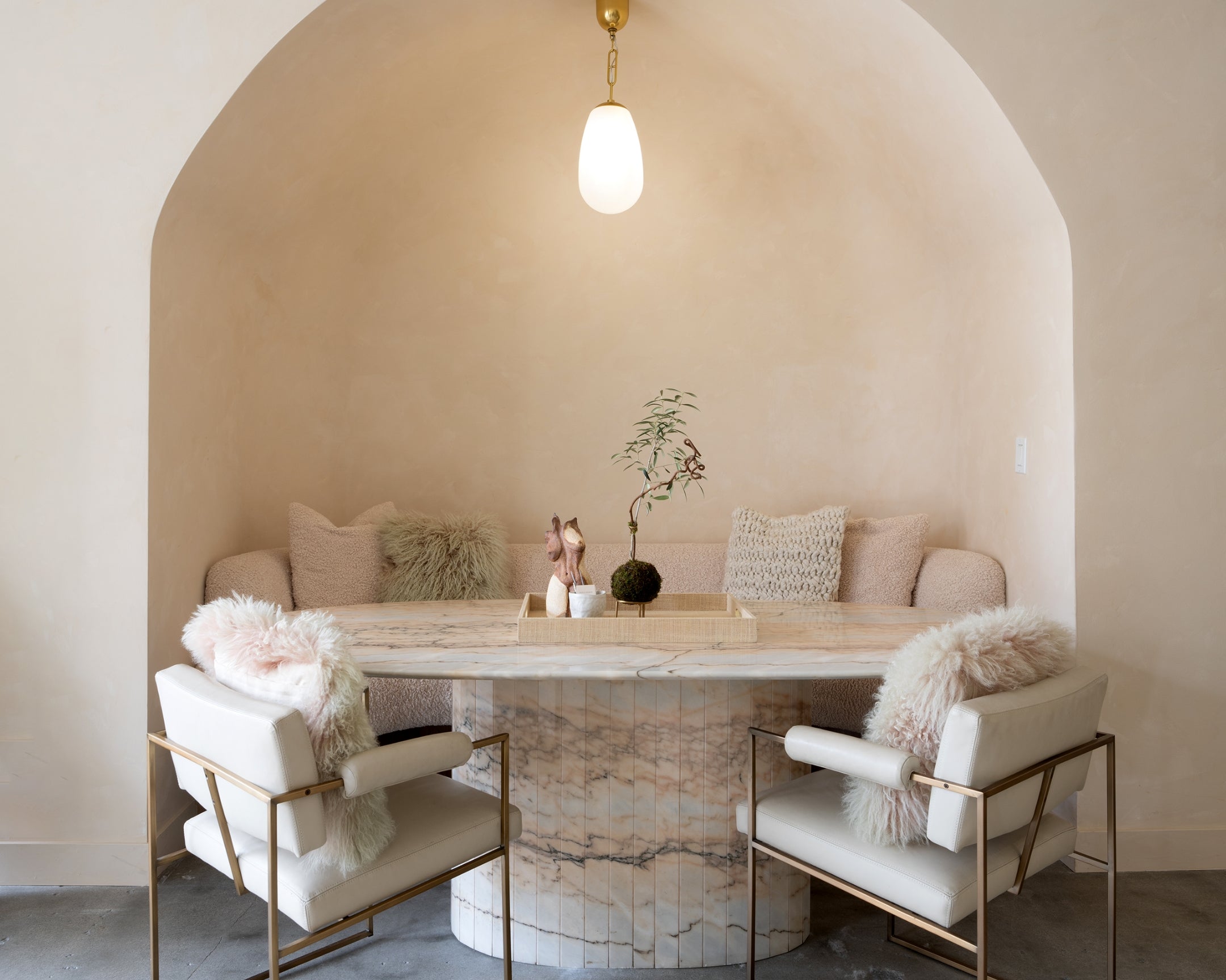 Modern living room with beige sofa, two white chairs, fluffy pillows, a marble table, and a hanging pendant light