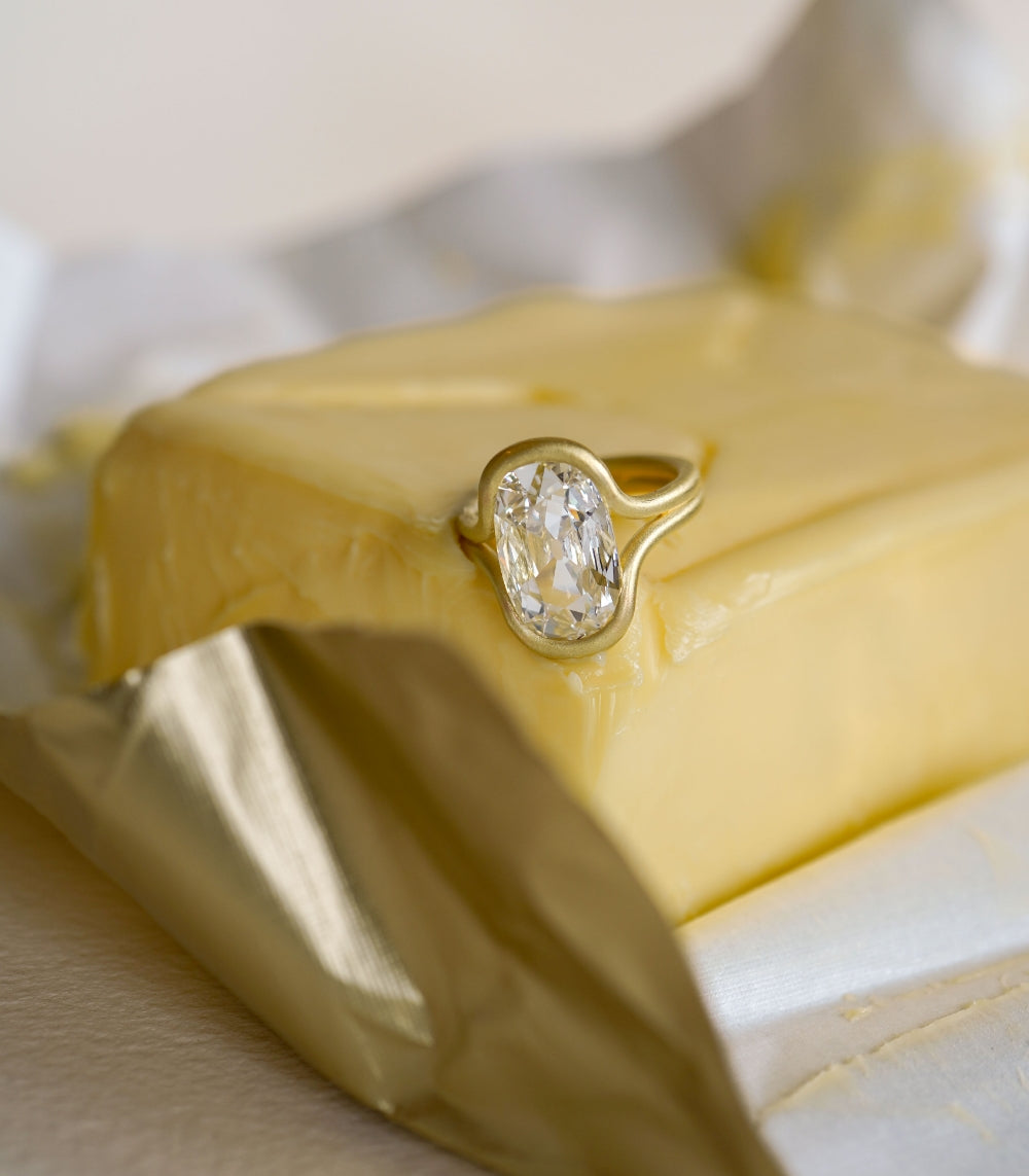 Onda SK-R114-LGD-FC-WD-4.03 unique engagement ring in gold with oval center stone on satin fabric