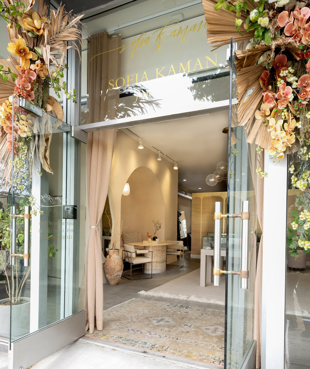 Storefront entrance with glass doors, flowing curtains, and colorful floral arrangements framing the display