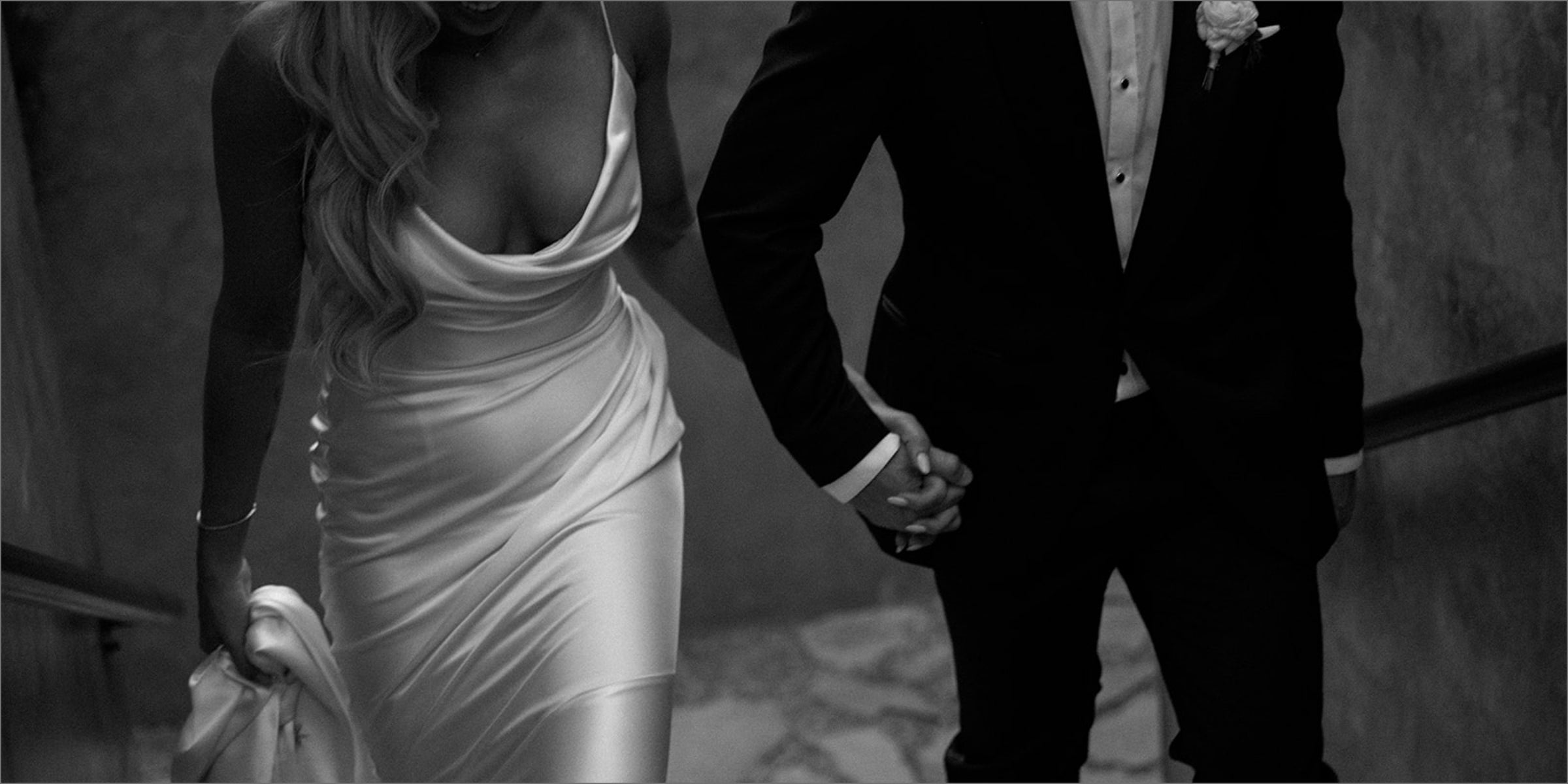 Understated black-and-white couple holding hands, asymmetrical embrace, wedding-party scene indoors