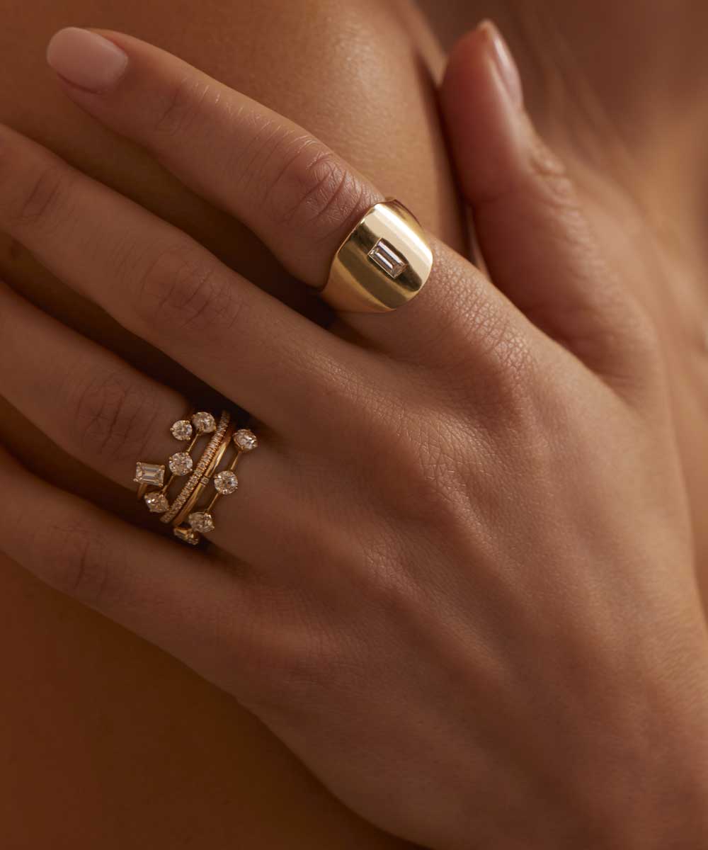 Unique engagement ring stacked on fingers—understated gold bands with small channel and round stones.