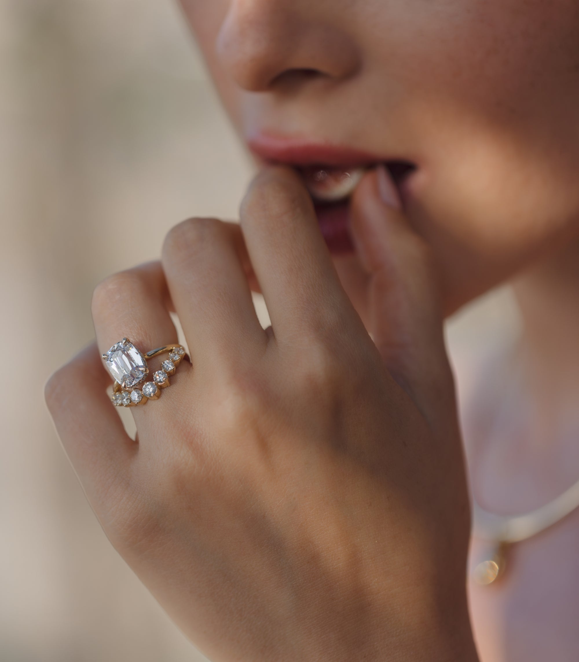 Unique engagement ring with a large clear diamond on a gold band, close to a softly blurred face