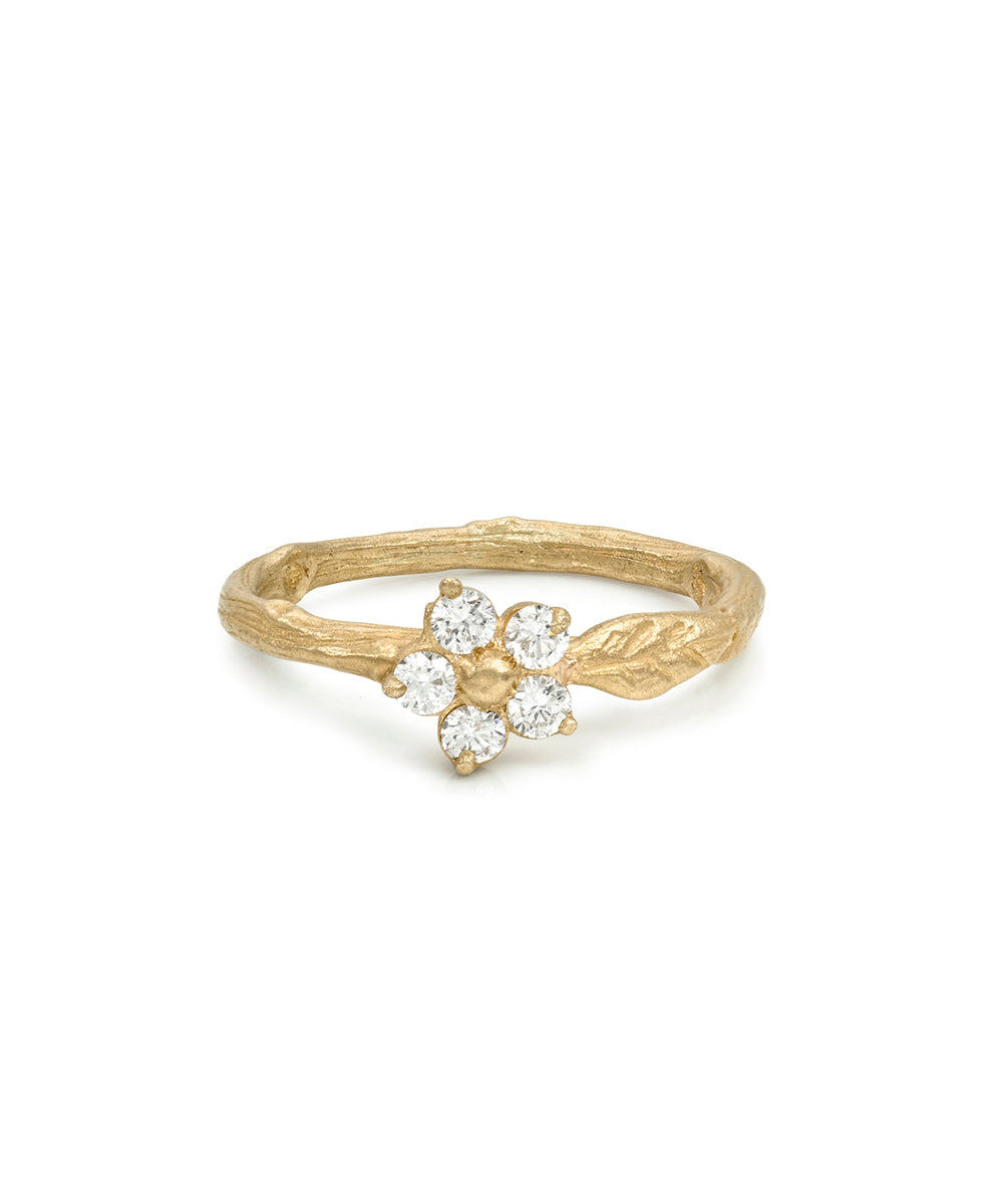A gold ring designed like a flower bud growing from a textured branch, featuring five clear round-cut gemstones, shown on a plain white background.