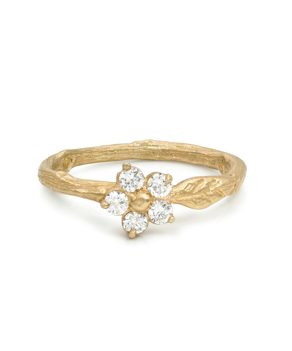 A gold ring featuring a textured, branch-like band with a small flower motif set with five clear round-cut gemstones, photographed on a clean white background.