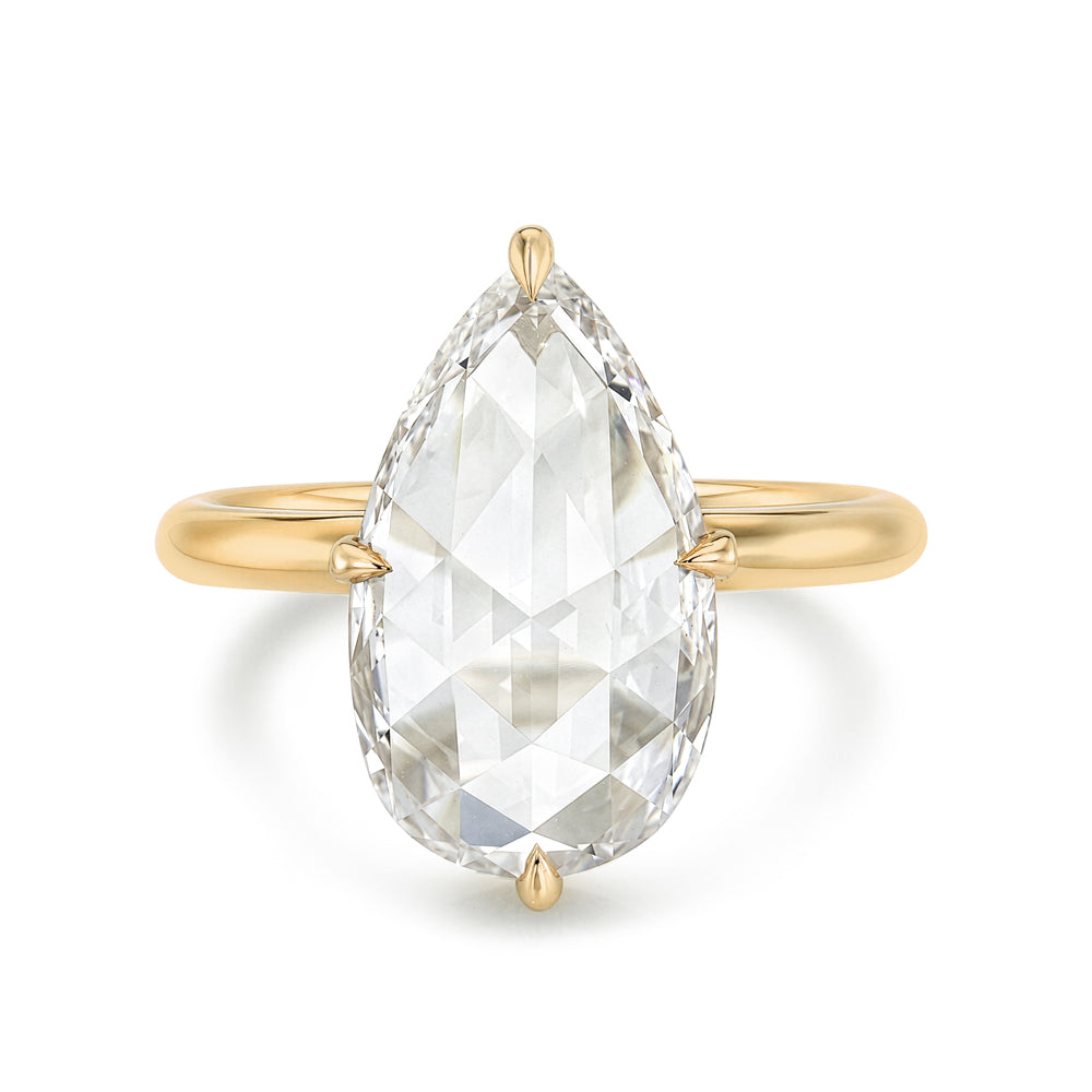A yellow gold ring featuring a large, rosecut pear shaped diamond in a four-prong setting, shown against a plain white background.