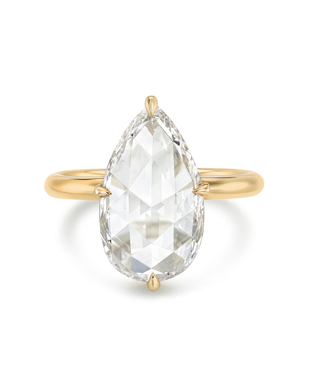 A yellow gold ring featuring a large, rosecut pear shaped diamond in a four-prong setting, shown against a plain white background.