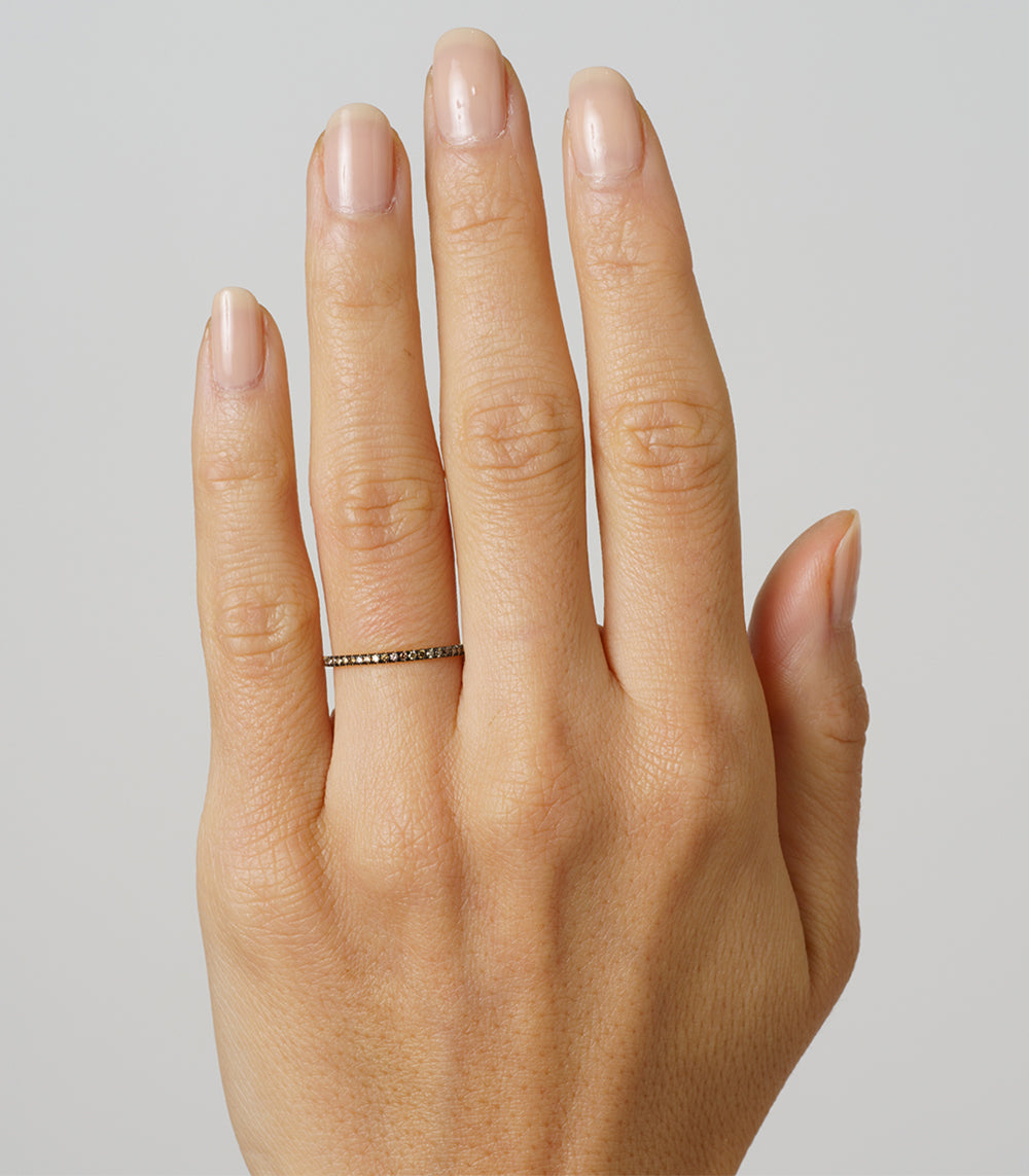 De Vil by EB-R12 gold band ring with fine pavé stones, understated sparkle on a hand against light gray.