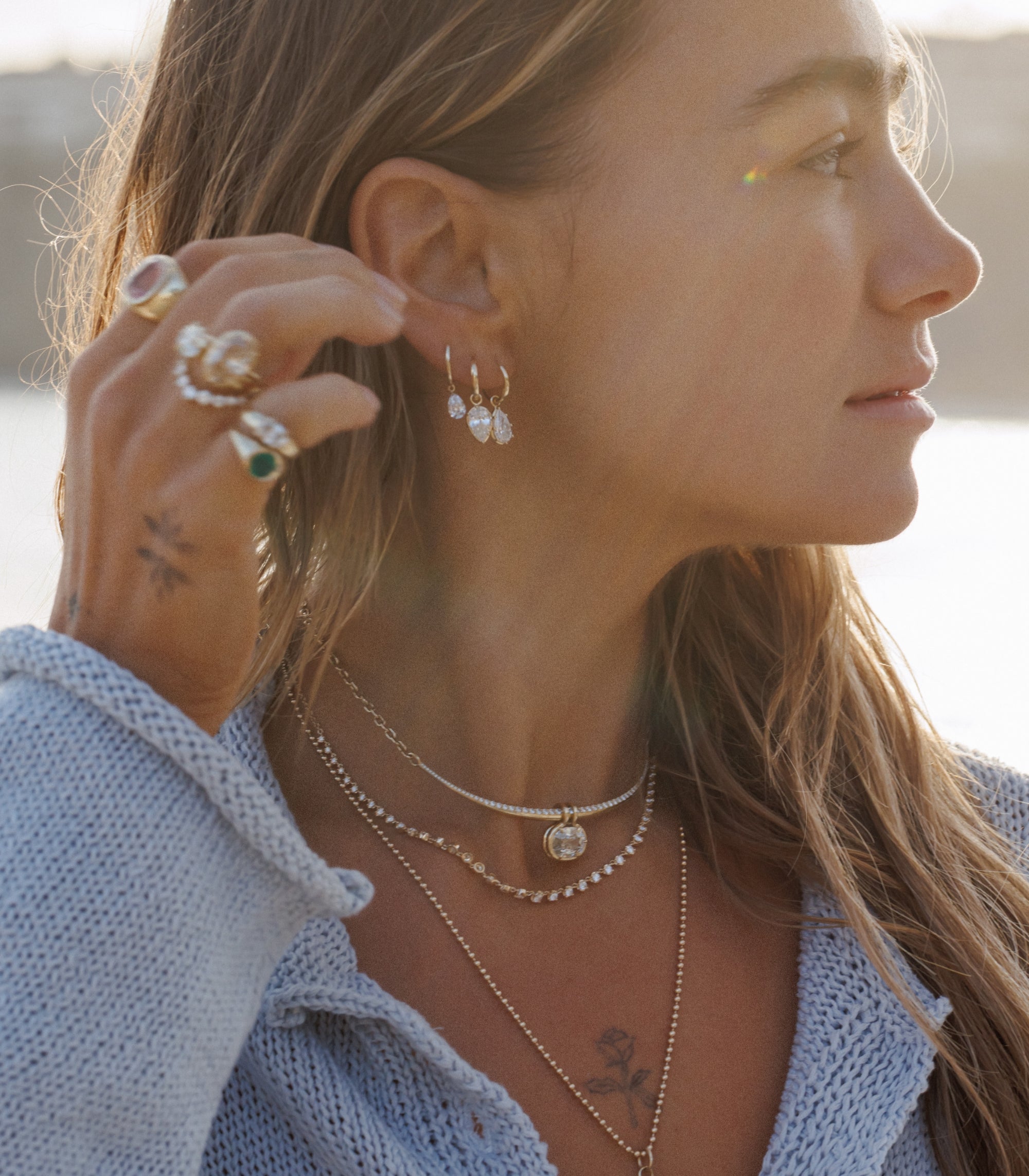 Brunette Woman On Beach With Sun Behind Her Showing Off Gorgeous Ring And Earring Stack Of Solid Gold Fine Jewelry