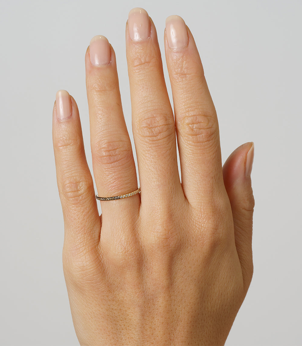 De Vil EB-R12 14K yellow gold band ring on a hand with a fine stone-studded edge under soft light
