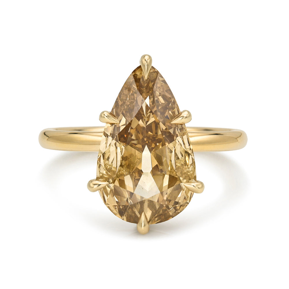 A pear-cut champagne diamond ring in a yellow gold setting on a plain white background.