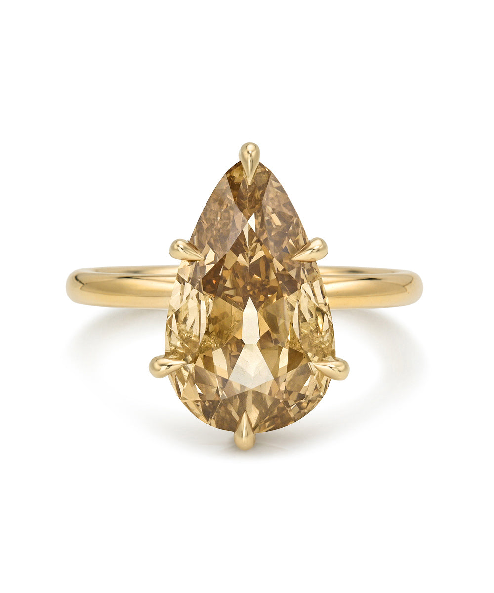 A pear-cut champagne diamond ring in a yellow gold setting on a plain white background.