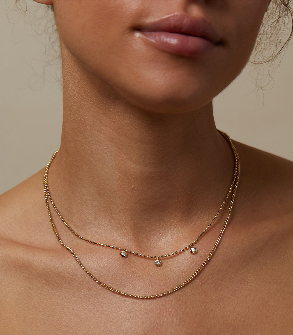 The Sexy CN-C10 layered gold necklace with tiny round stones and dangling charms on a delicate chain