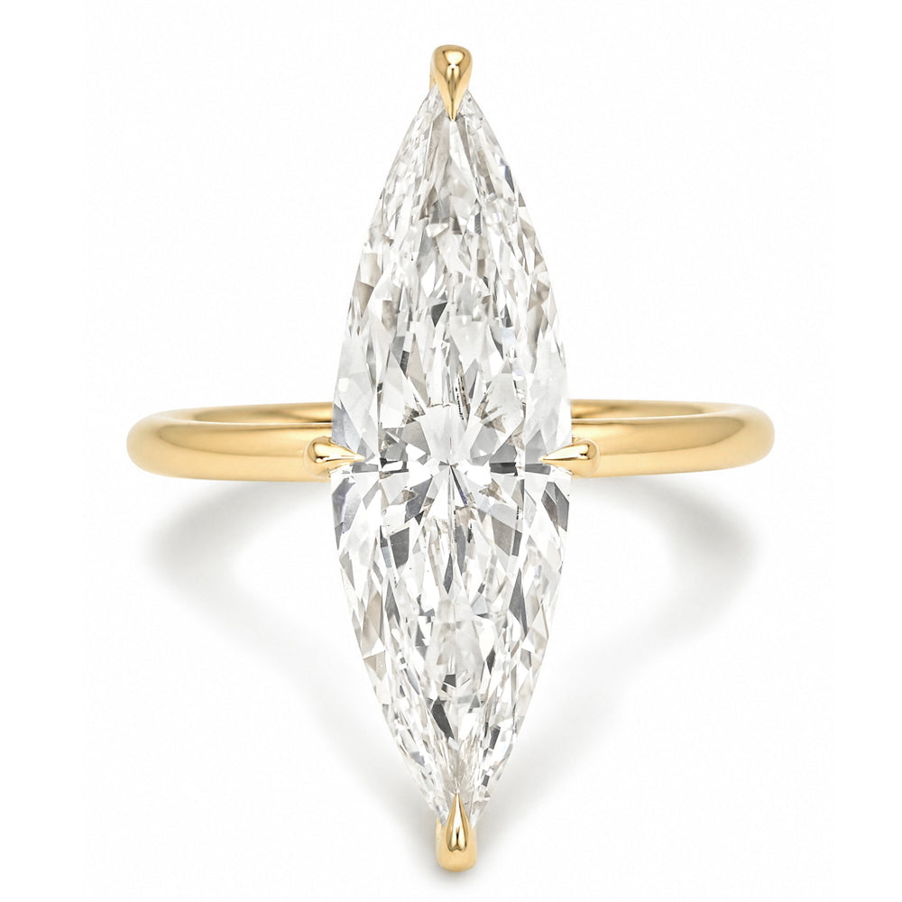 A yellow gold ring featuring a large marquise brilliant-cut diamond set vertically in the center. The diamond is held by a delicate four-prong setting on a polished gold band, photographed against a clean white background with a soft shadow.