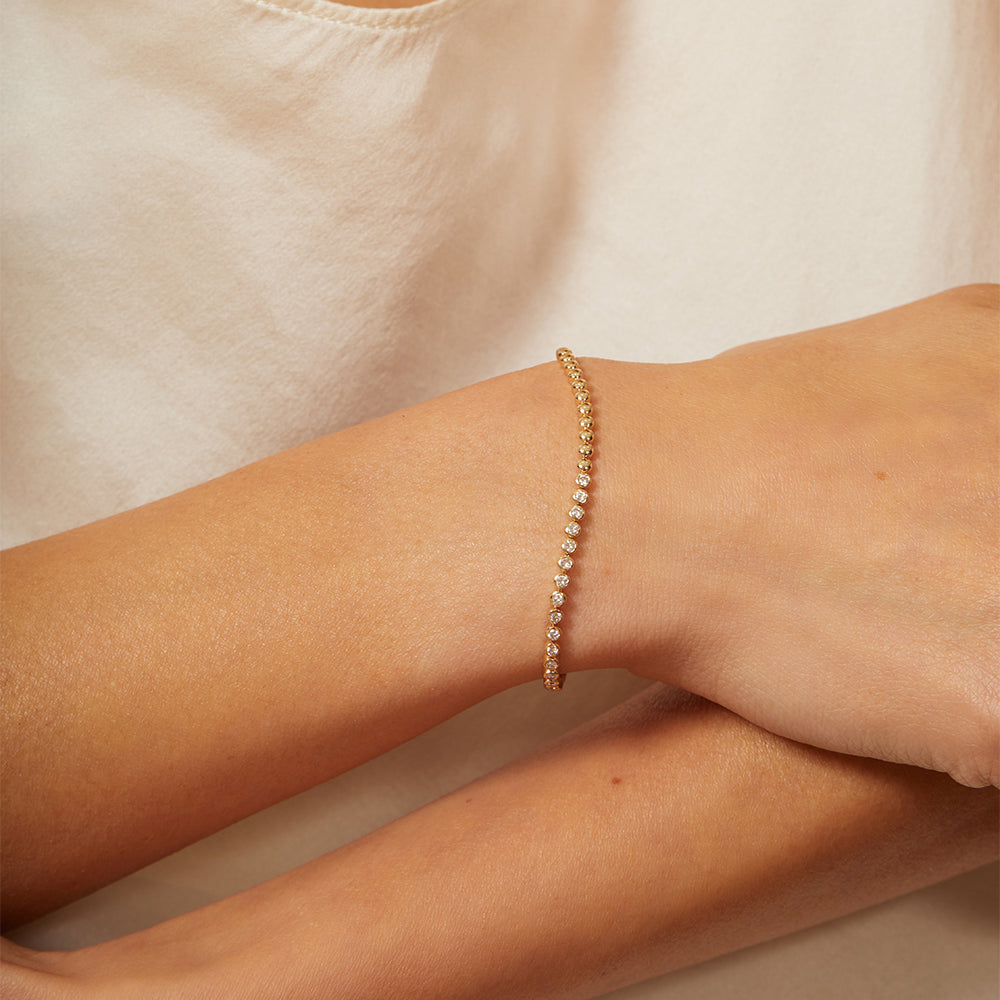 'Bu II' CC-DB5 gold bracelet with pavé stones, understated sparkle on a wrist resting on fabric