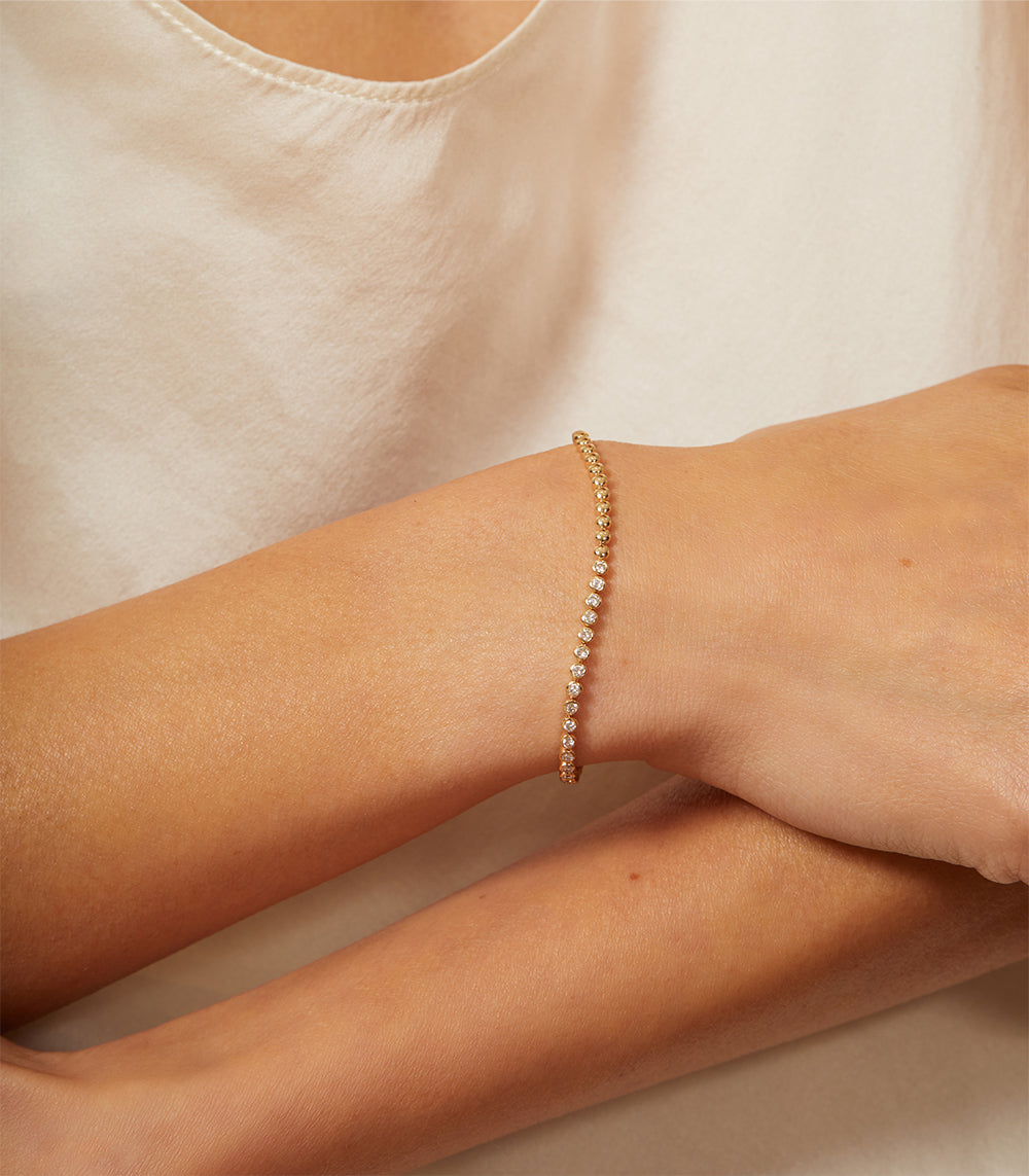 'Bu II' CC-DB5 gold bracelet with pavé stones, understated sparkle on a wrist resting on fabric