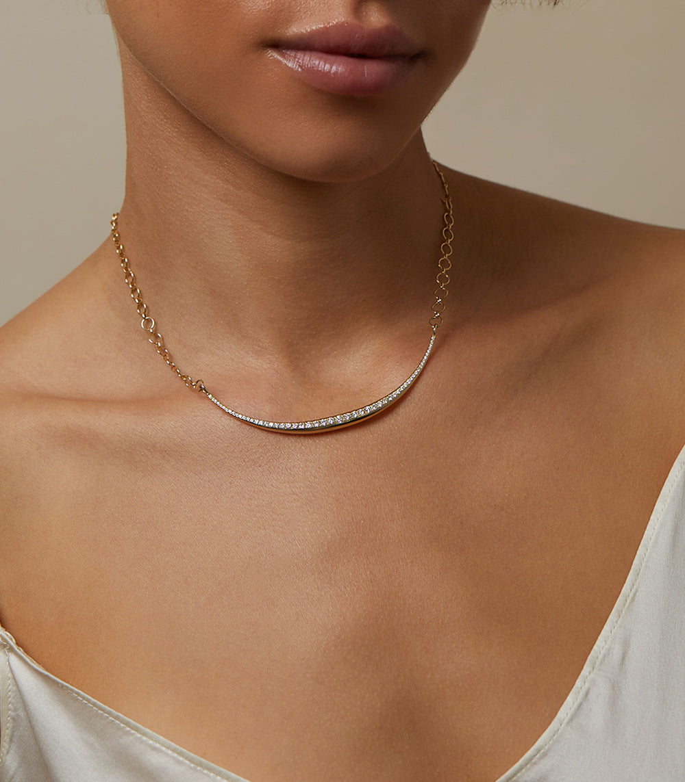 The Luna SK-N4 gold necklace with a curved diamond-studded bar, close-up on collarbone.