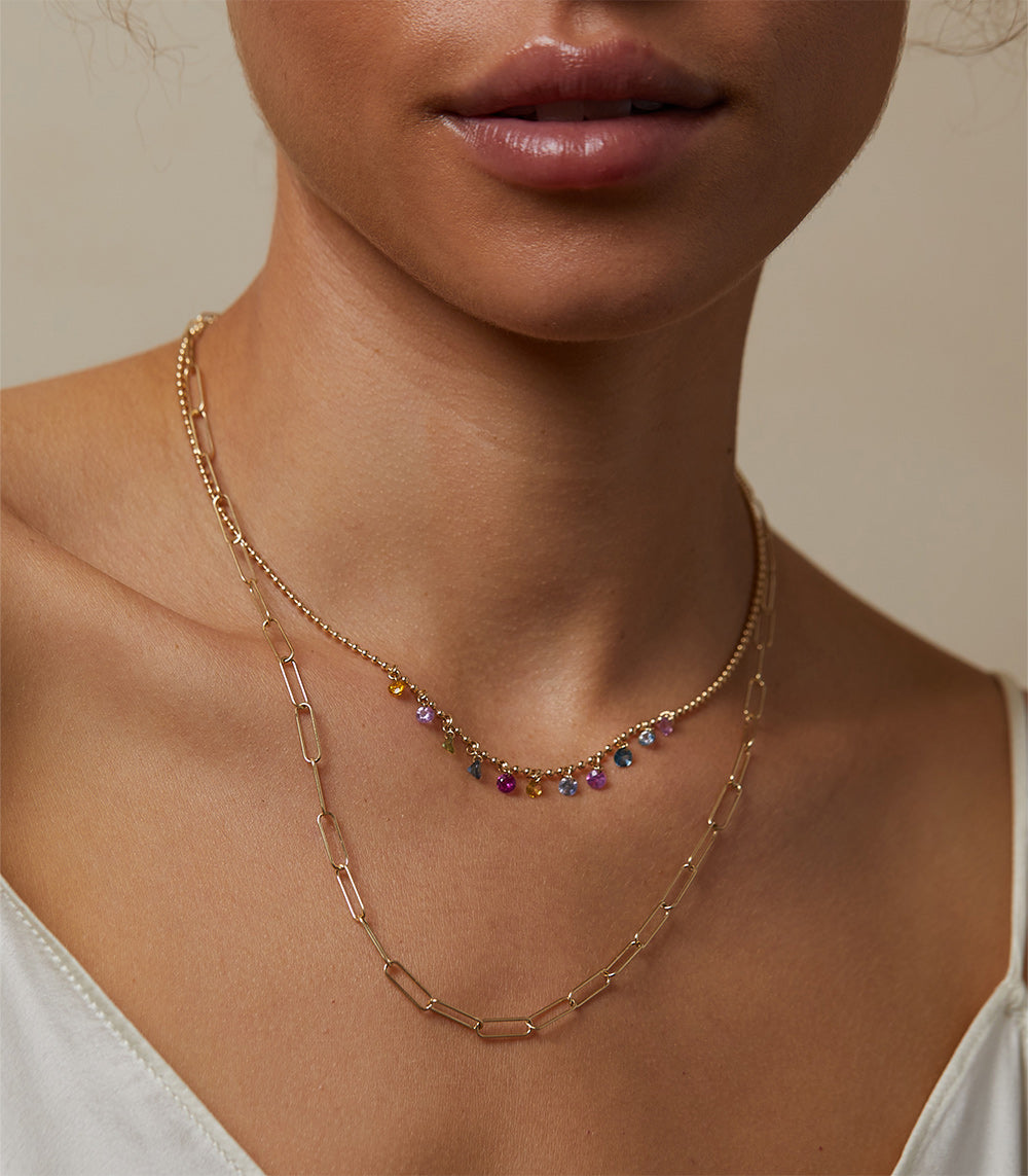 The Crush CN-C9 layered gold necklace with multicolor gemstone beads at the collar, close-up on neck.