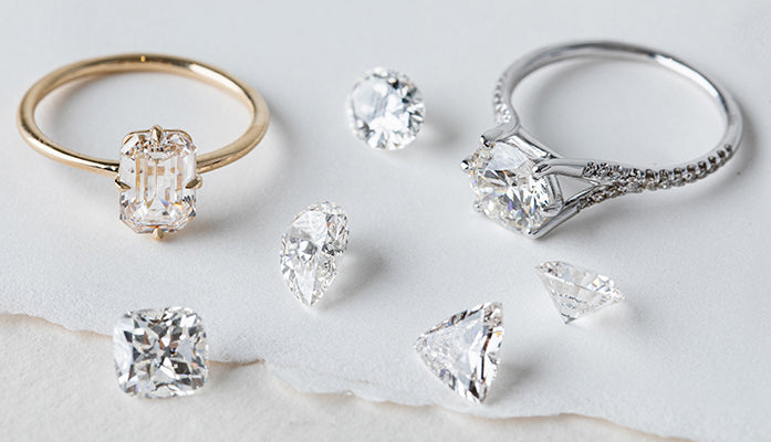Unique engagement ring with an asymmetrical setting, gold and silver bands beside loose diamonds on white fabric