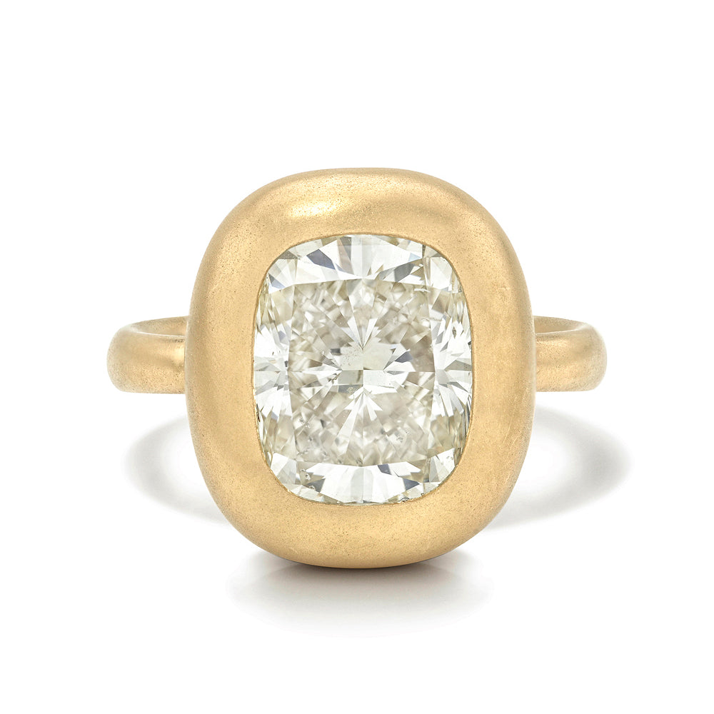 A yellow gold ring featuring a large, cushion-cut diamond center stone in a rounded bezel setting, shown on a clean white background.